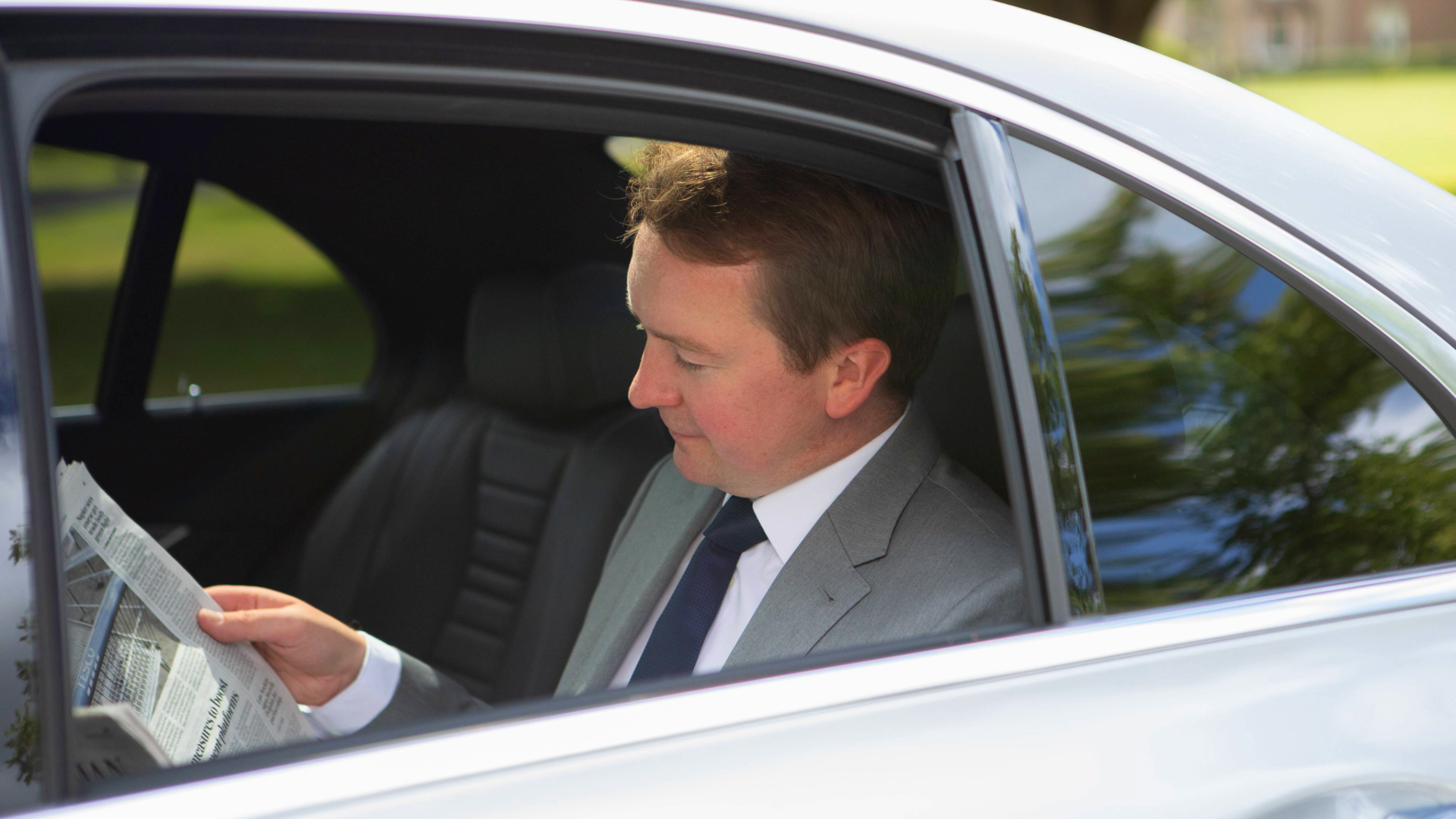 Business passenger in back of Mercedes-Benz E-Class reading newspaper