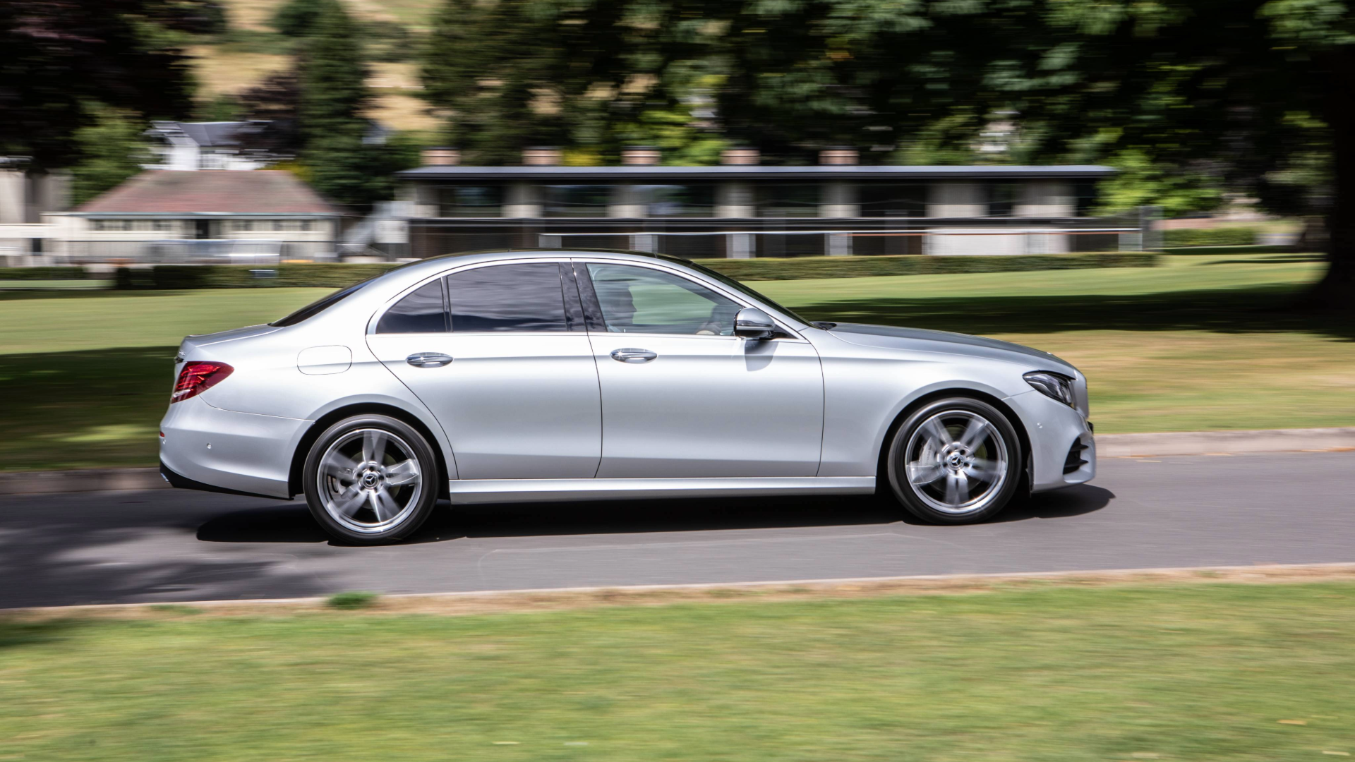 Silver luxury sedan car driving on a suburban street with green lawns and houses in the background