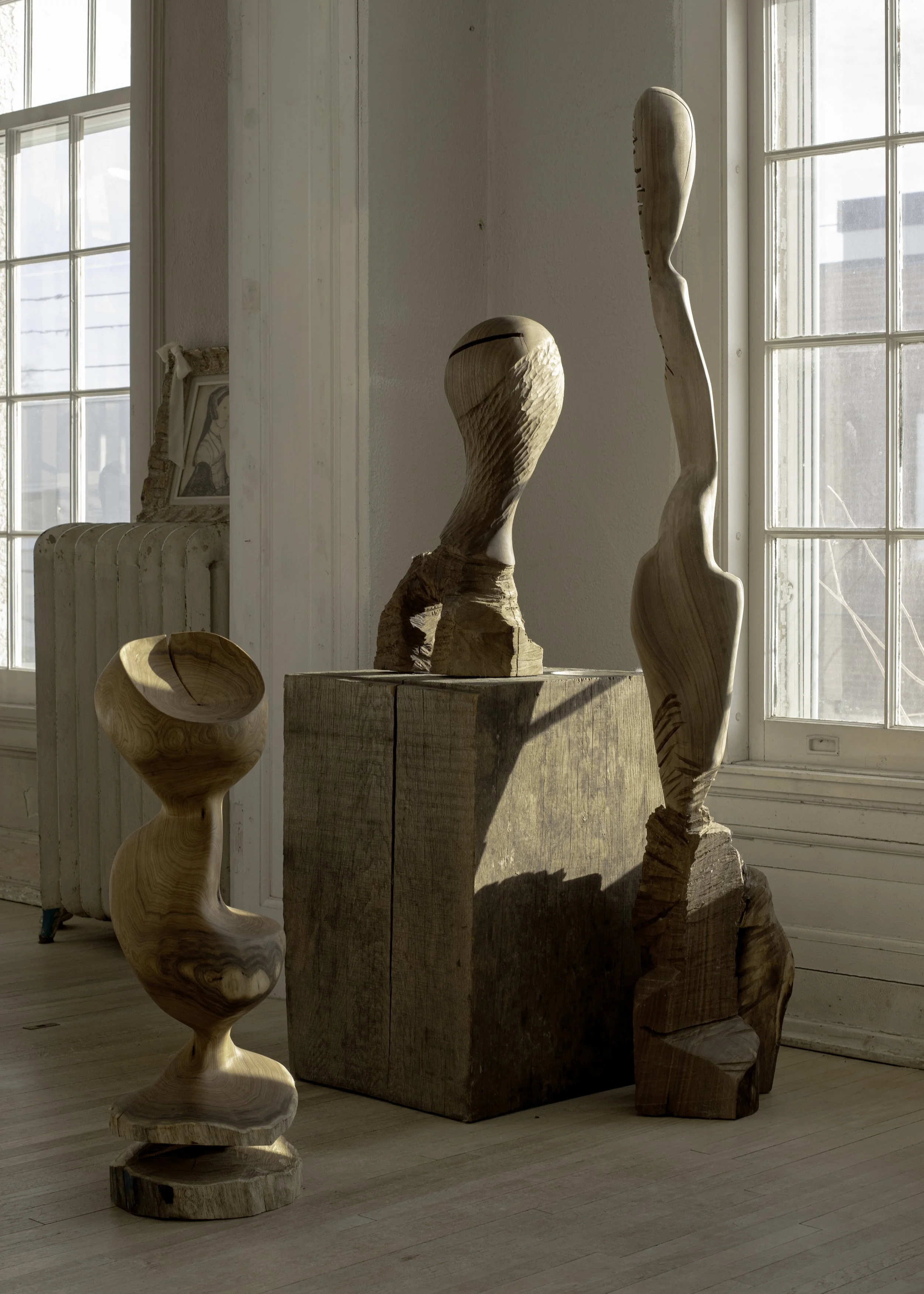Indoor art display featuring wooden sculptures and a framed picture on a windowsill, with sunlight illuminating the scene.