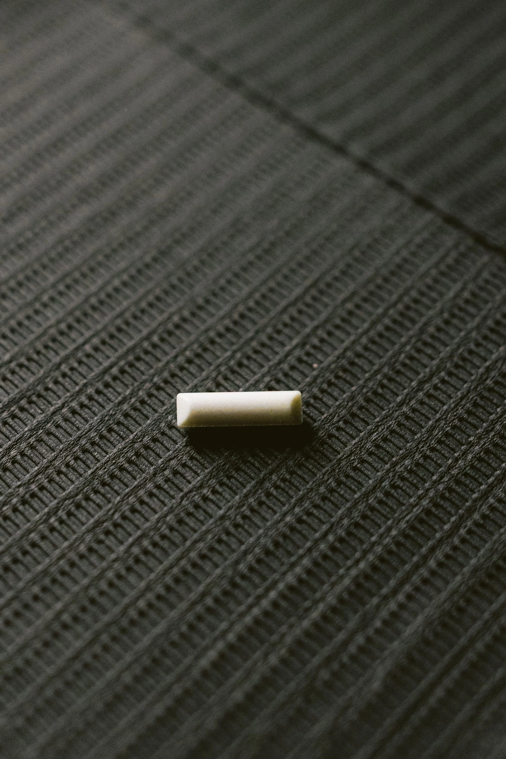 A small, white rectangular object lying on a textured, dark grey surface.