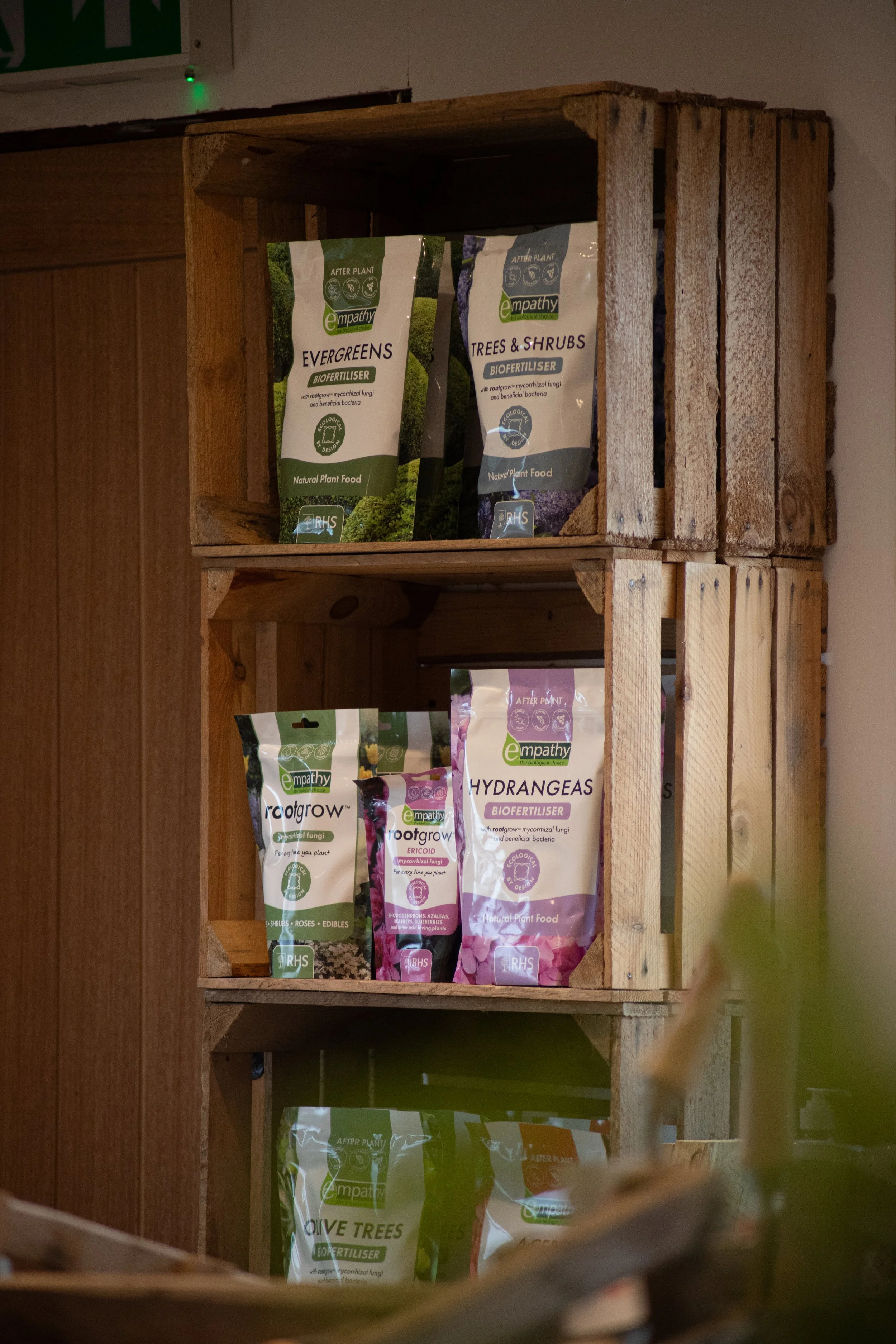Wooden crate shelves holding various bags of plant fertilizers labeled for different types of plants.
