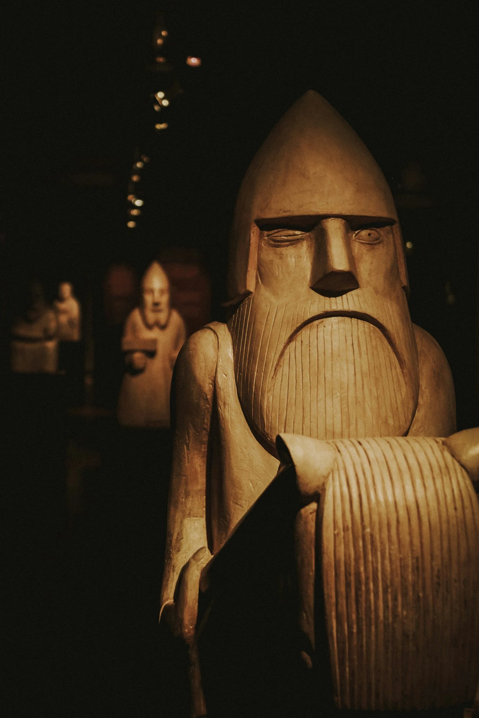 Wooden sculptures of historical or religious figures arranged in a dimly lit display.