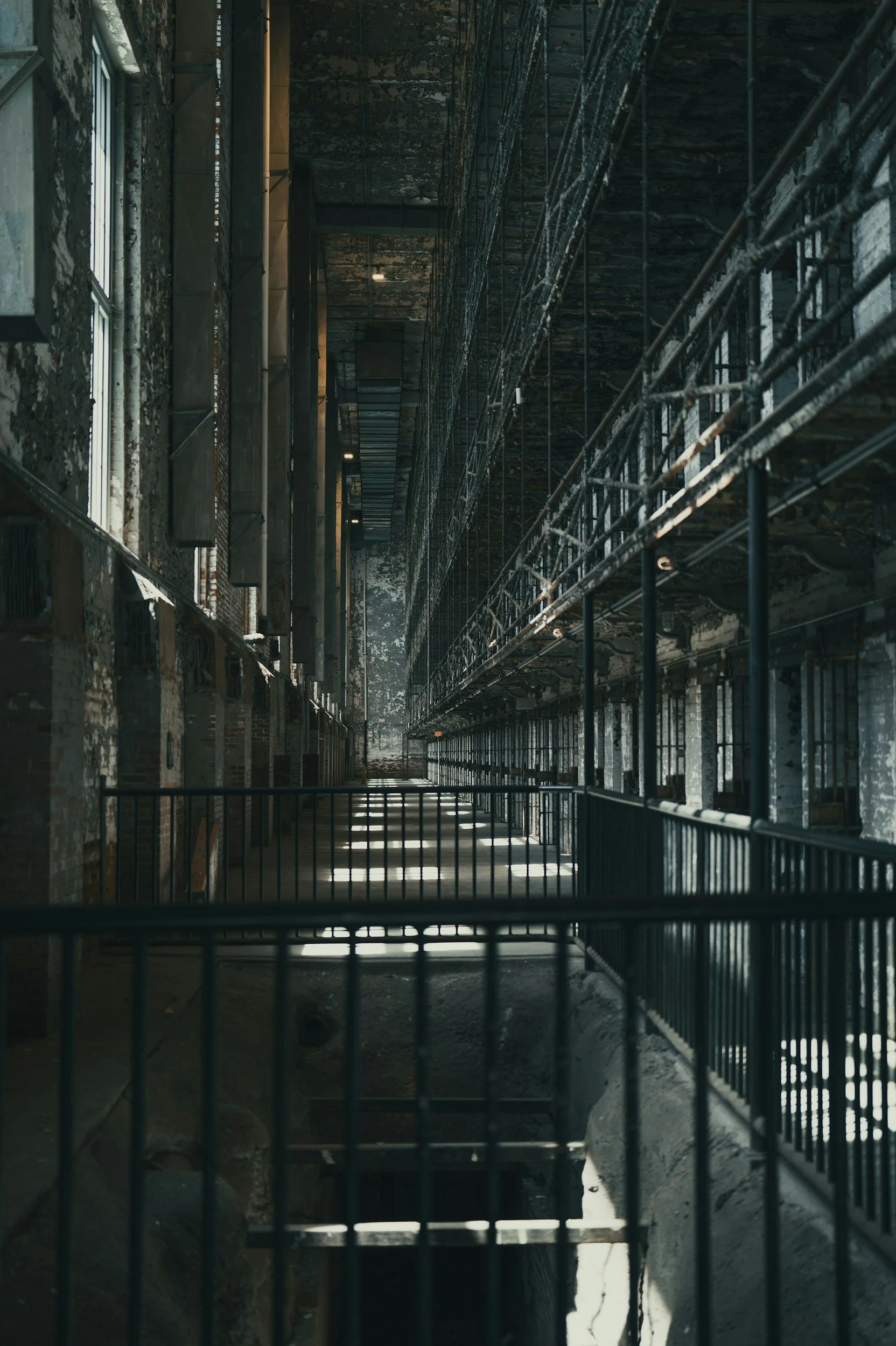 Interior of an abandoned or industrial building with rusted metal scaffolding, railings, and peeling paint on the walls, illuminated by natural light from windows.