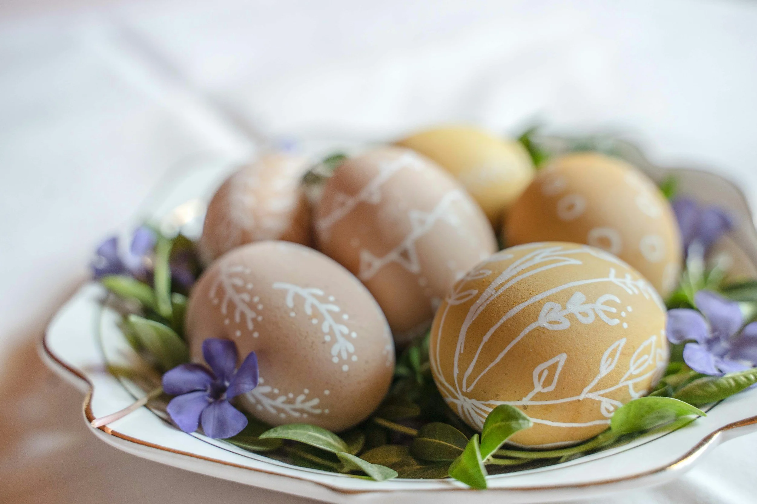 Decorated Easter eggs in a basket surrounded by purple flowers and green leaves.
