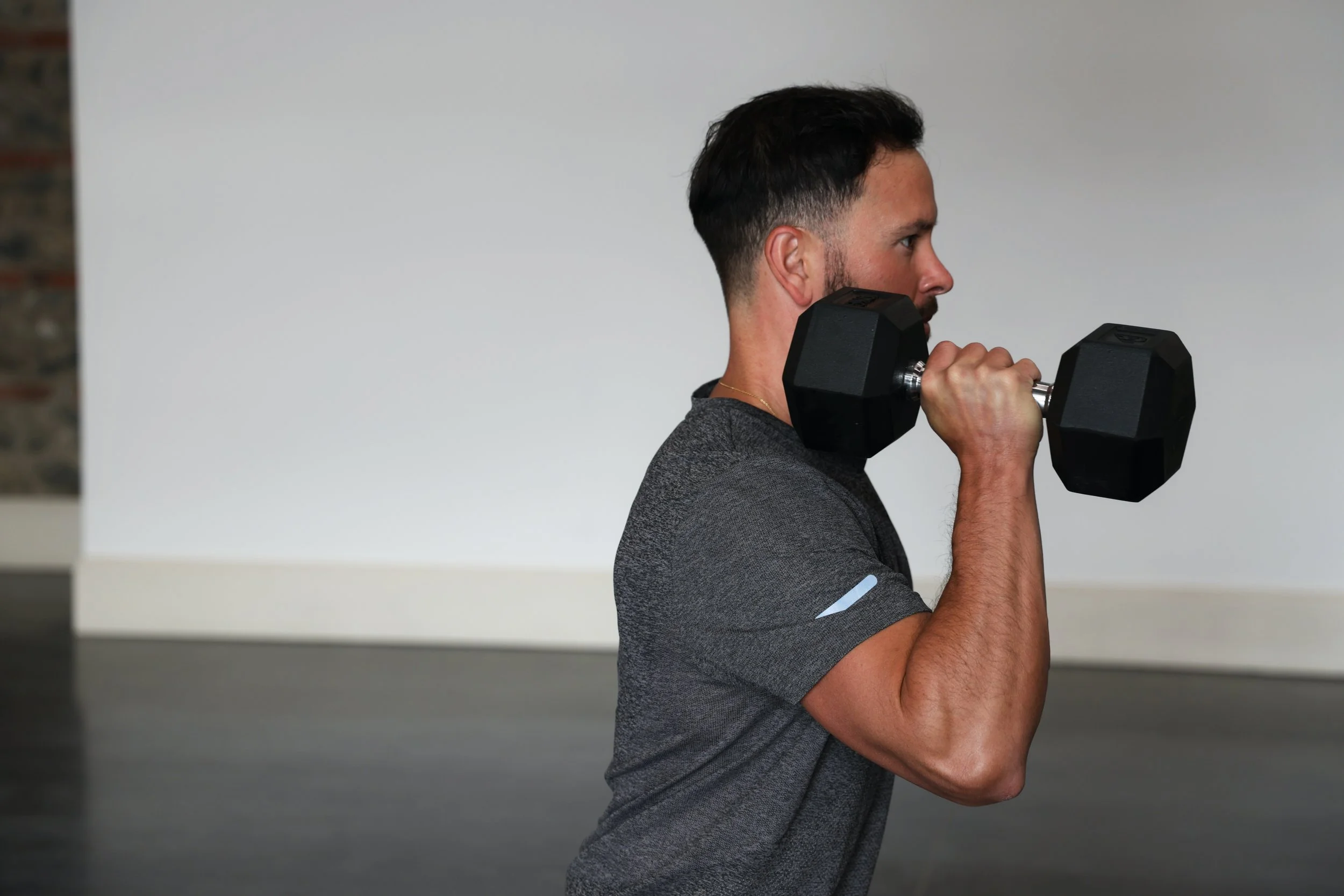 Homme faisant de l'exercice avec un haltère en position de curl biceps dans une salle de sport.