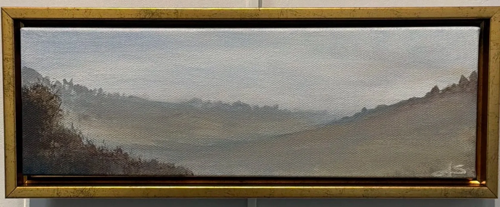 A landscape painting of misty mountains and valleys in muted colors, framed in wood.