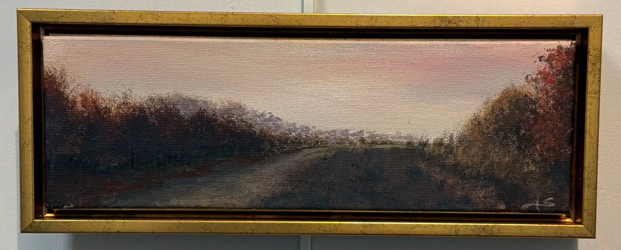 Painting of a peaceful road flanked by trees with autumn-colored foliage, under a pinkish dawn sky, framed in gold.