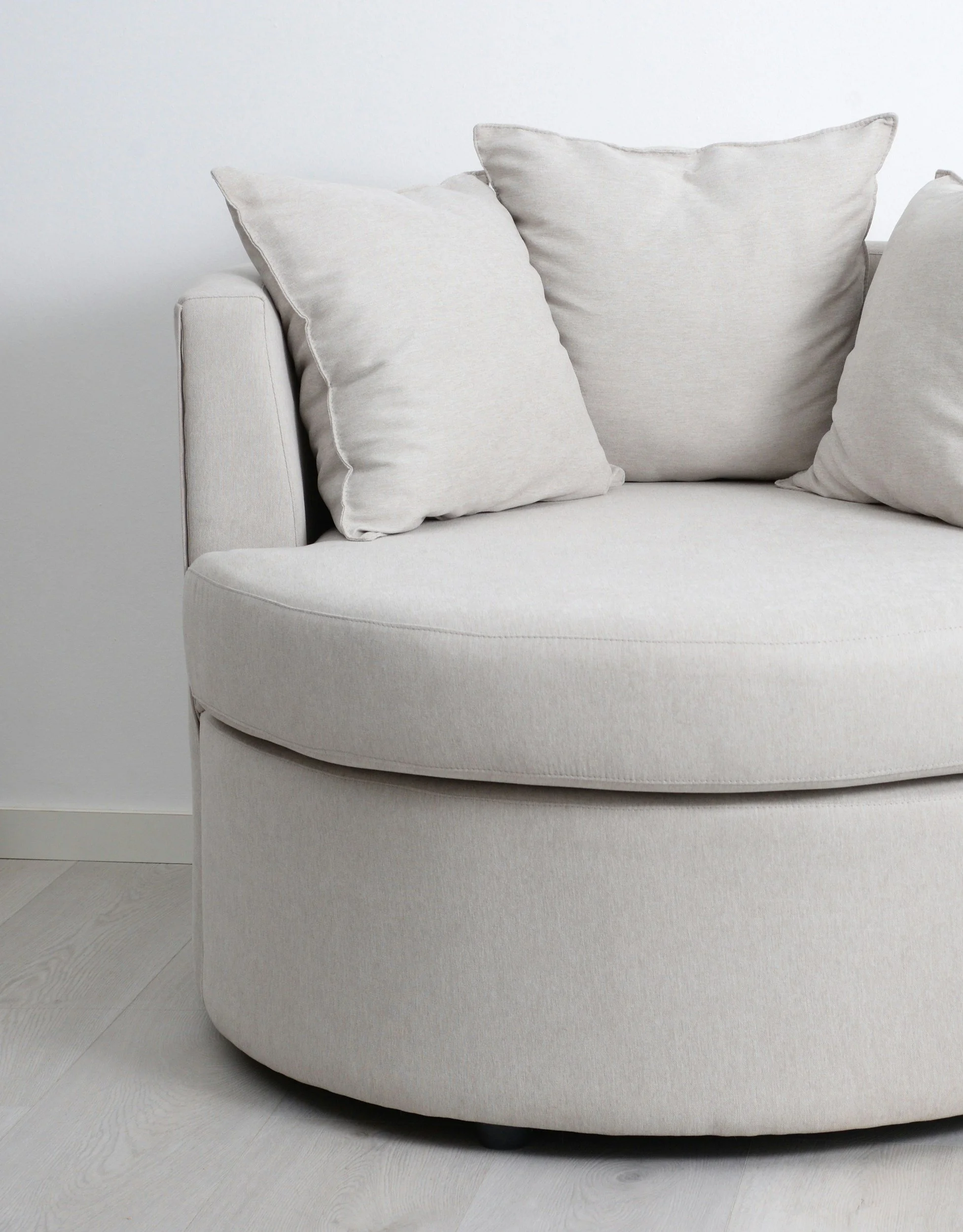 Close-up of a cream-colored upholstered sofa with three matching cushions on a light wooden floor and plain white wall in the background.