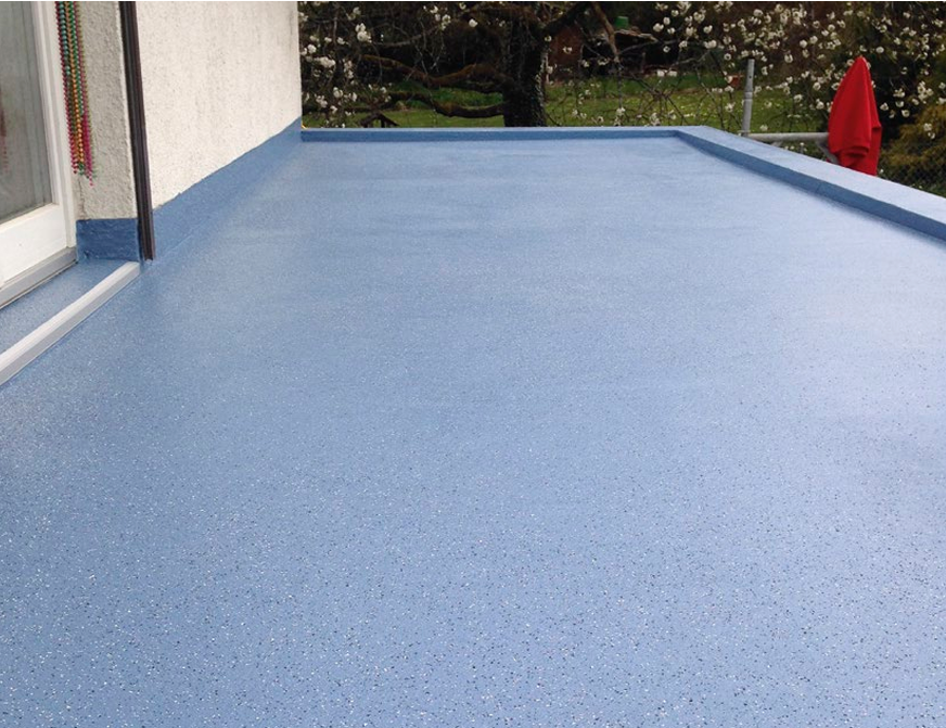 Terrasse en résine d'étanchéité liquide en bleu avec une surface lisse, à côté d'une maison avec une porte-fenêtre, en arrière-plan des arbres et un parasol rouge.