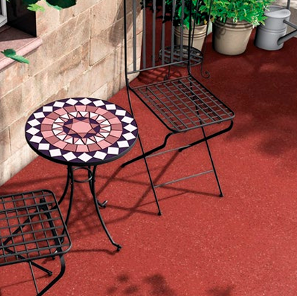 Deux chaises en métal noires avec assises en forme de grille et une petite table ronde avec un motif géométrique coloré sur un terrasse en résine d'étanchéité liquide extérieur.