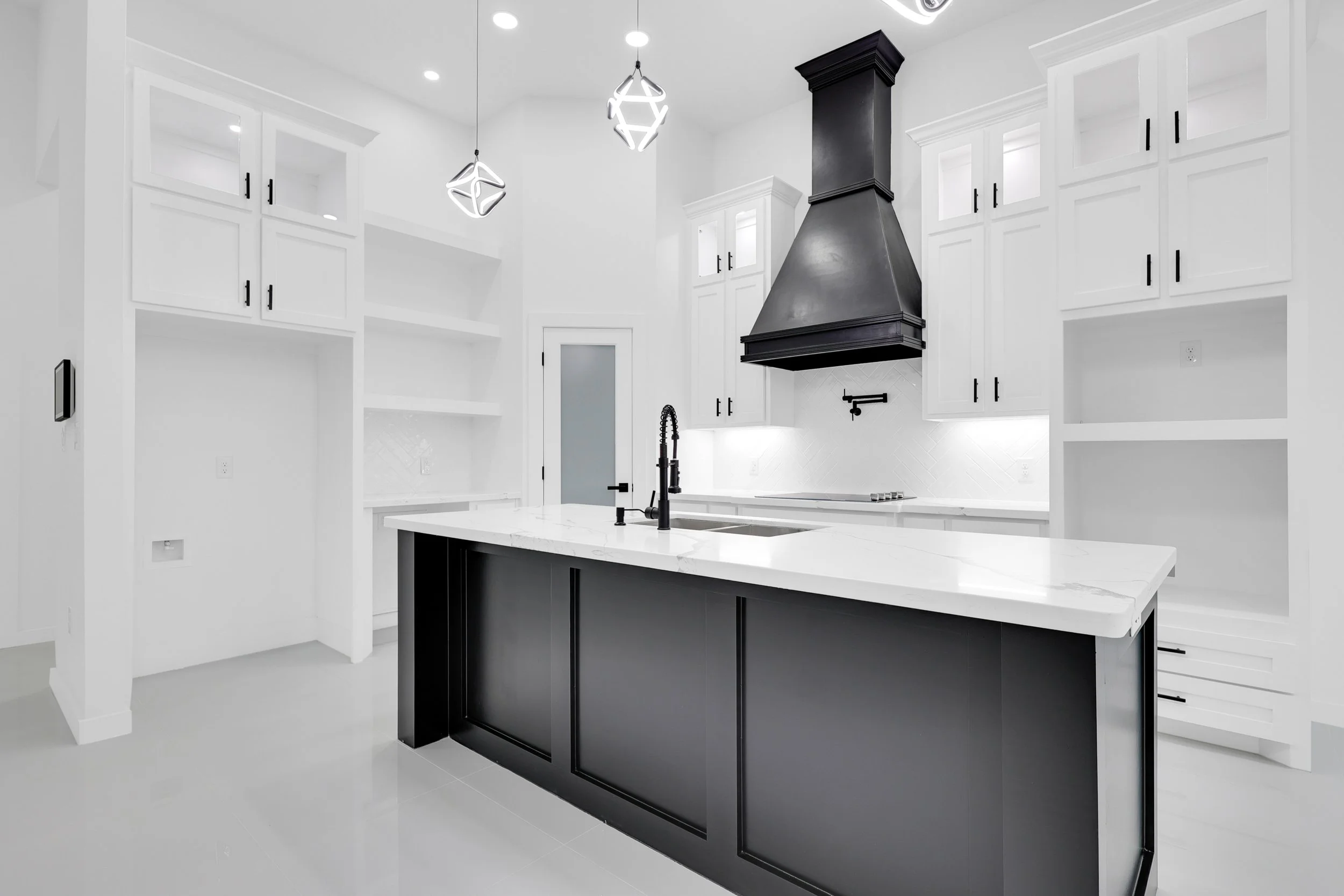 Modern kitchen with black and white design, featuring a black island, white cabinets, black range hood, and geometric pendant lights.