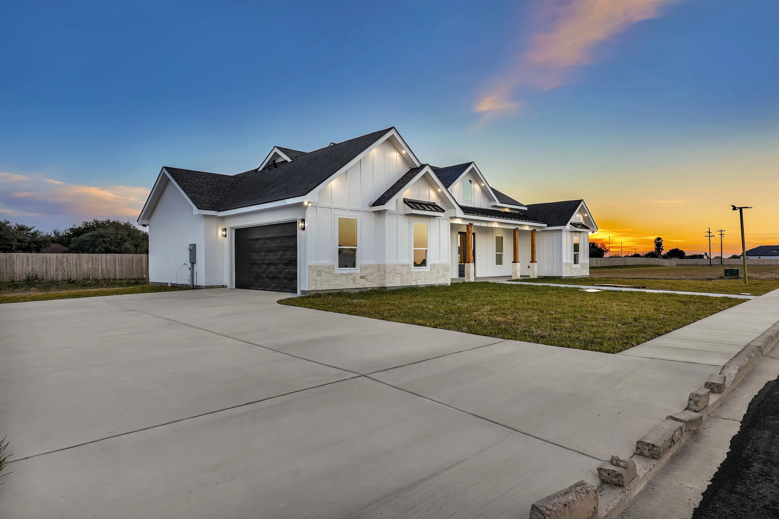 Modern white house with black roof at sunset, featuring a spacious driveway and well-maintained lawn.