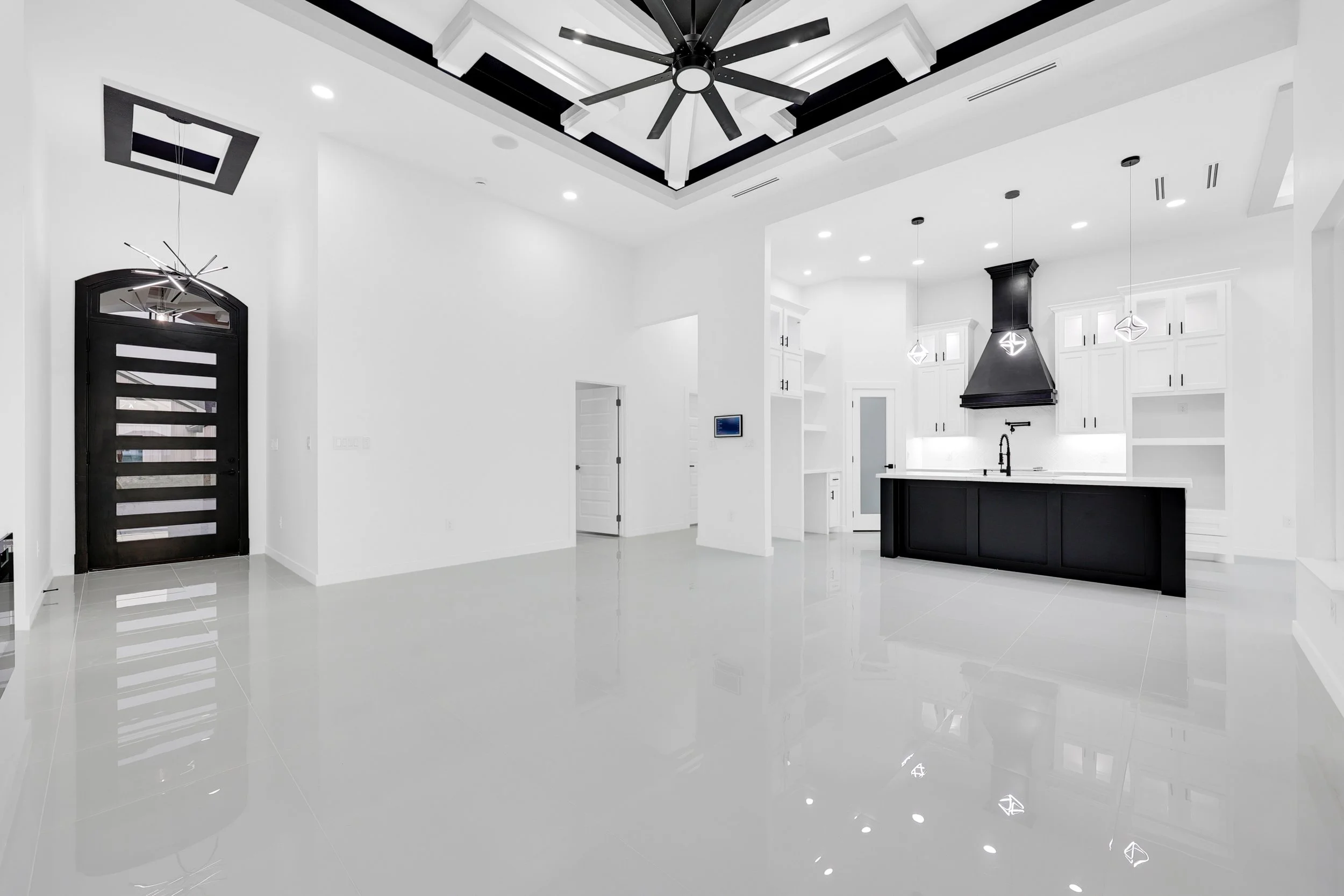 Modern white kitchen and living space with glossy floors, large black ceiling fan, and stylish black and white cabinetry.