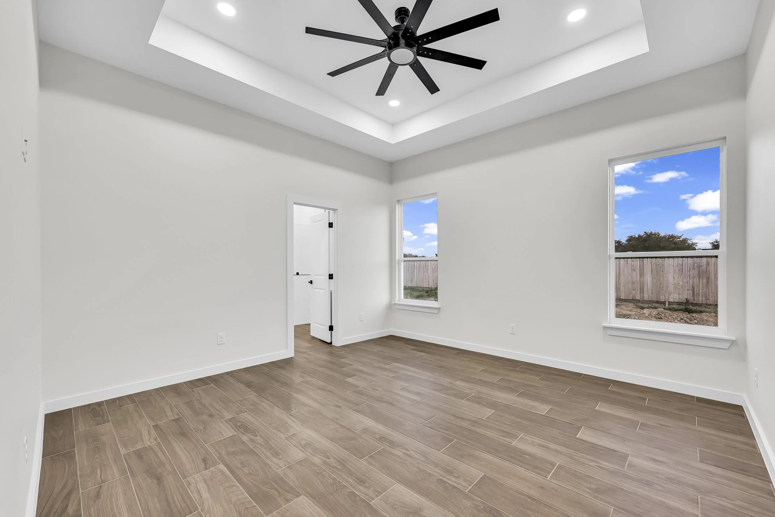 Empty room with wood floor, ceiling fan, recessed lighting, and large windows.