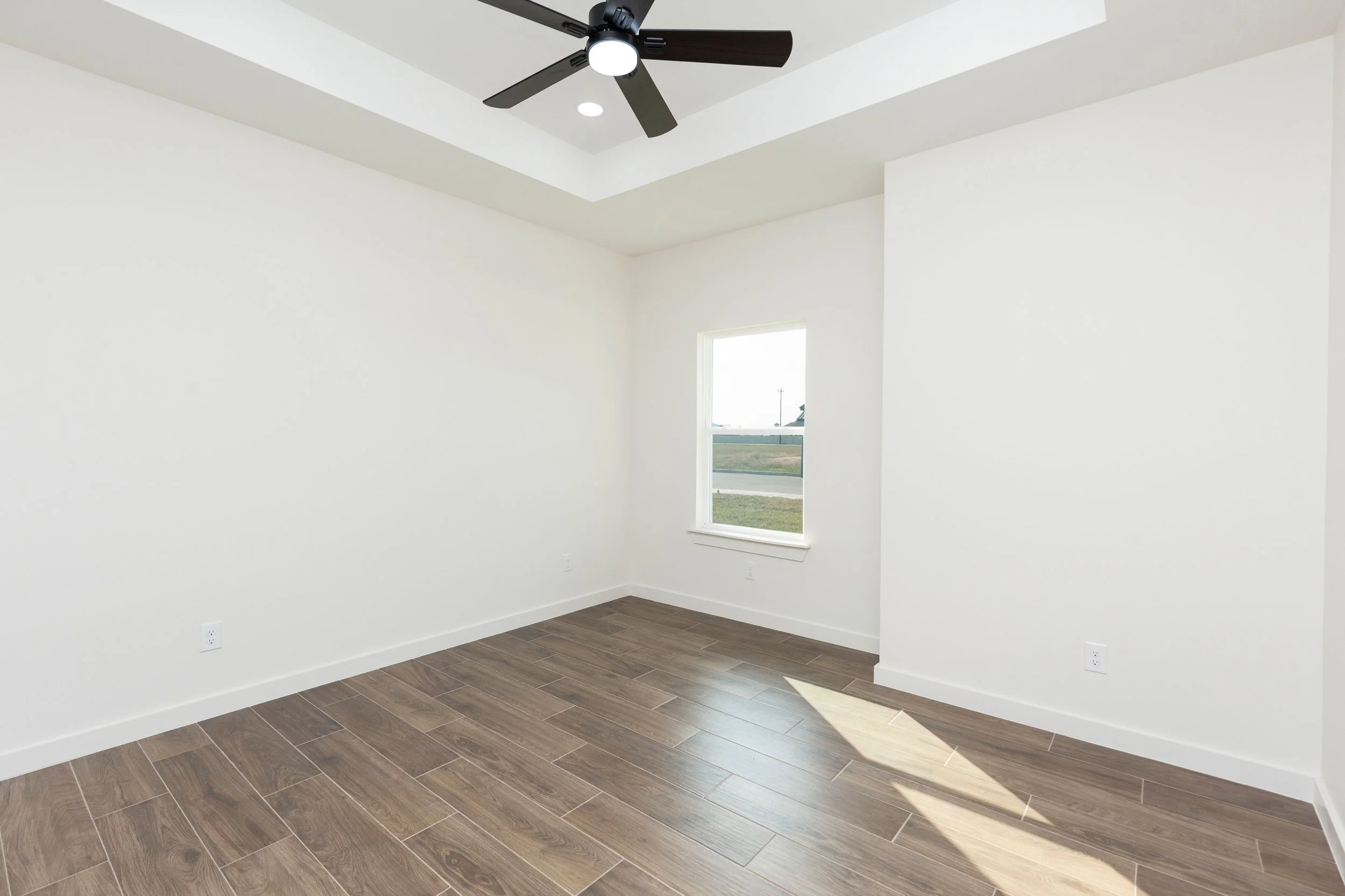Empty room with white walls, a wooden tile floor, a ceiling fan, and a window.