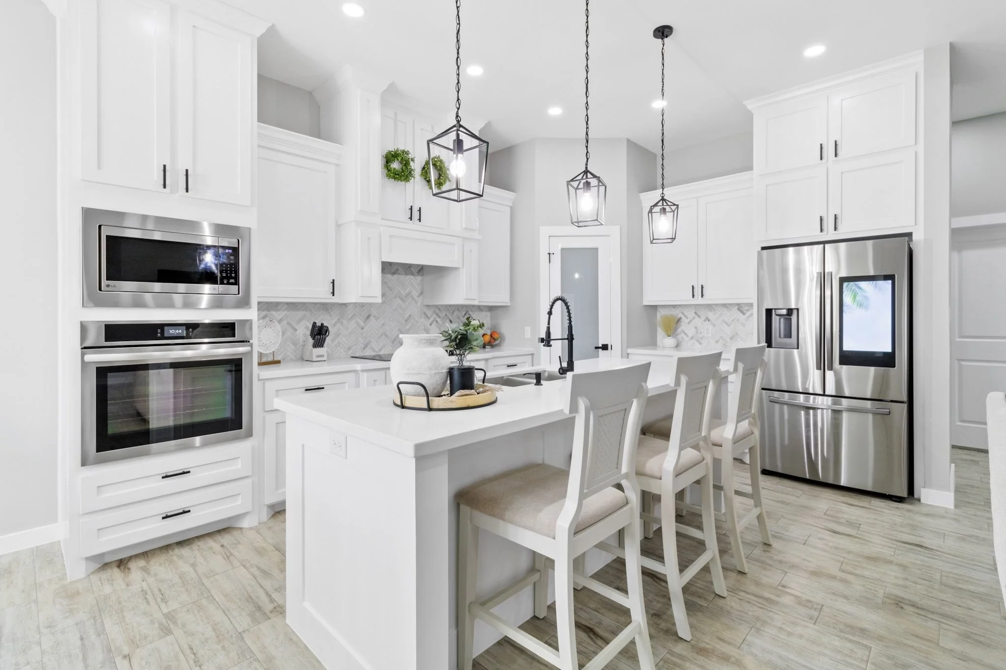 Modern white kitchen with island, stainless steel appliances, pendant lights, and bar stools.