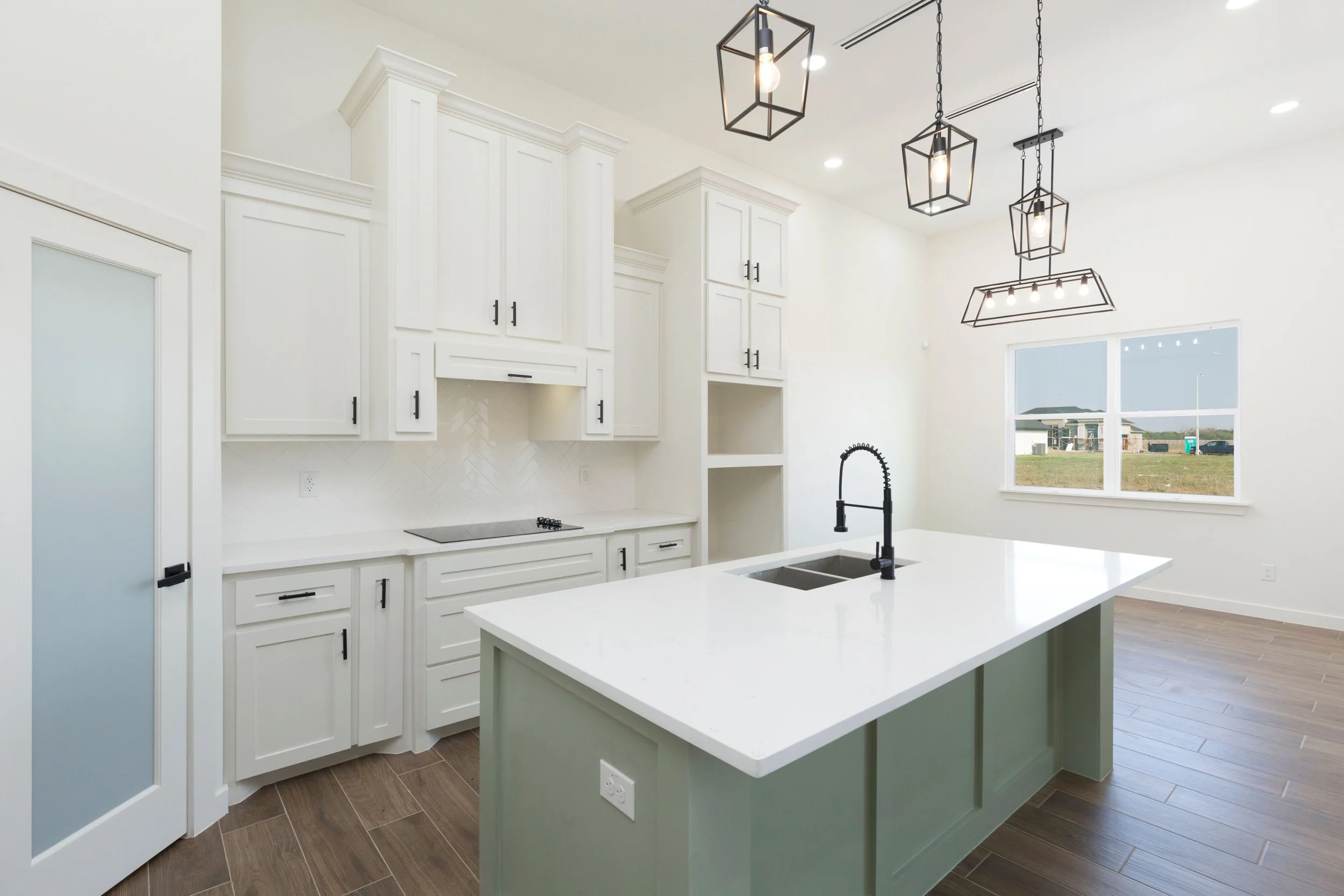 Modern kitchen with white cabinets, central island with sink, black fixtures, wooden floor, and hanging pendant lights.