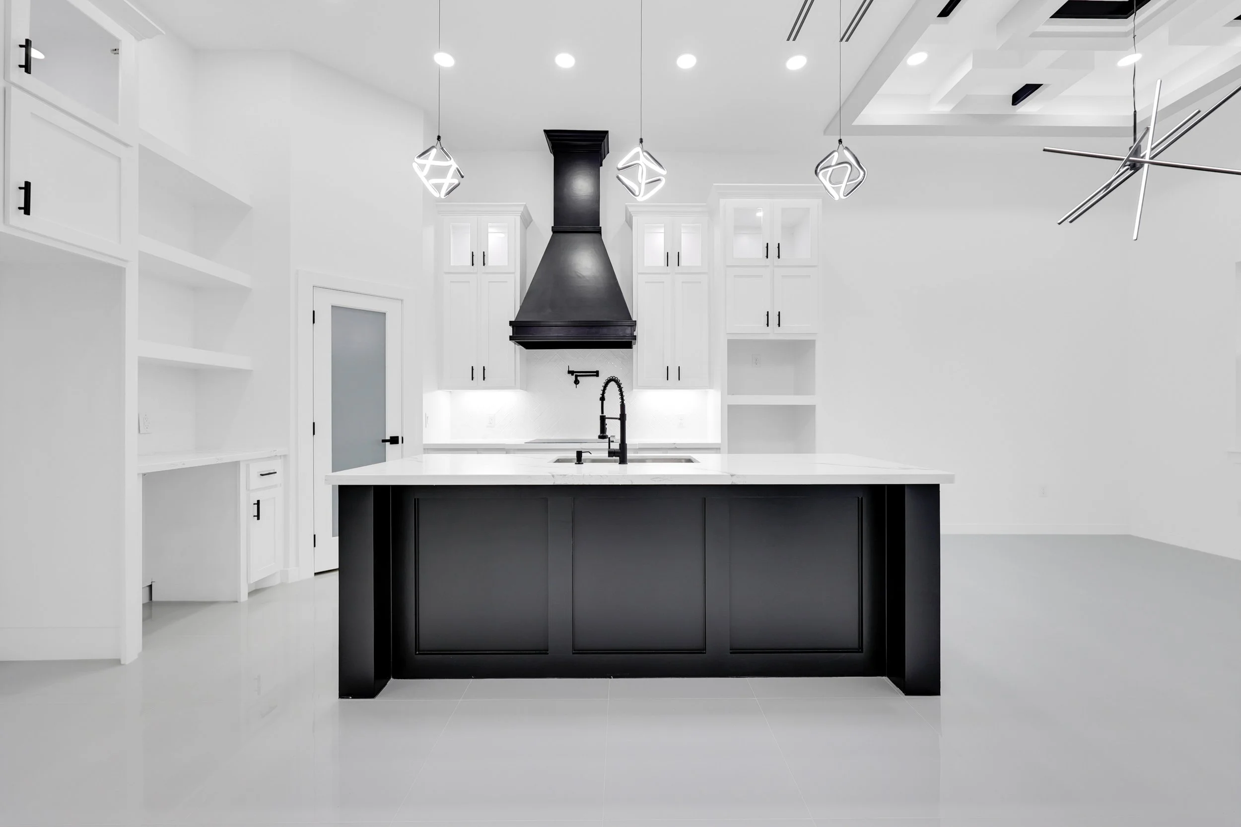 Modern kitchen with black island, white cabinets, unique pendant lighting, and a black range hood.