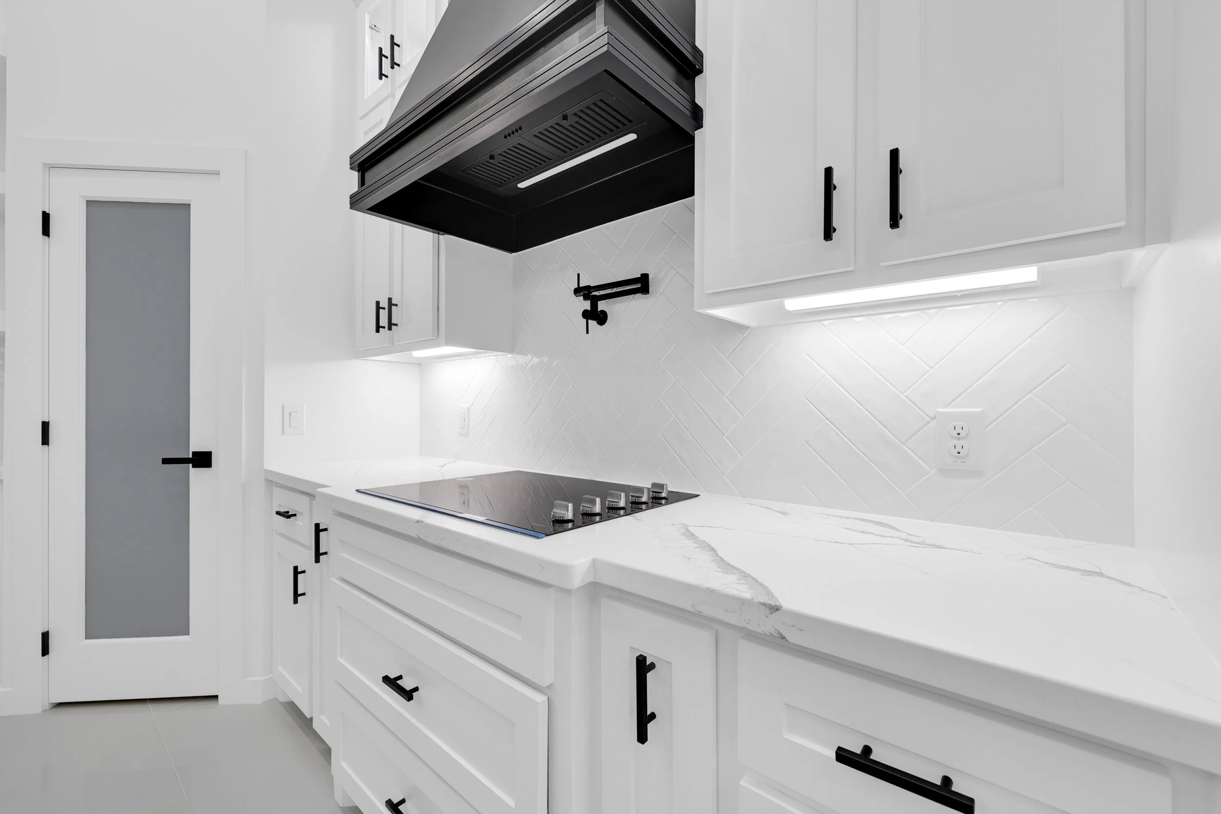 Modern white kitchen with black appliances, bright interior, and clean minimalistic design.