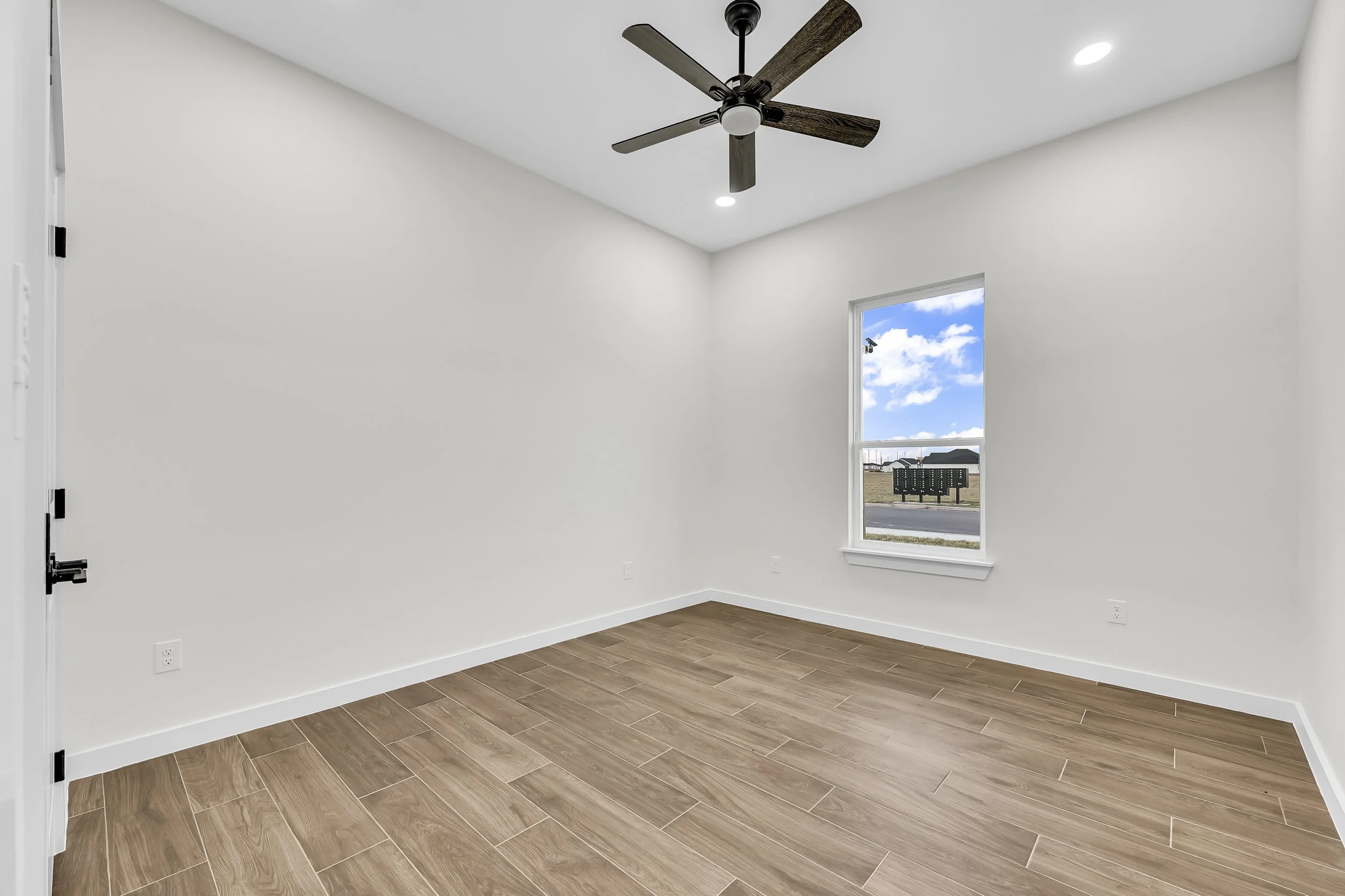 Empty room with wood-look tile flooring, a ceiling fan with lights, and a window with a view of the outdoors.