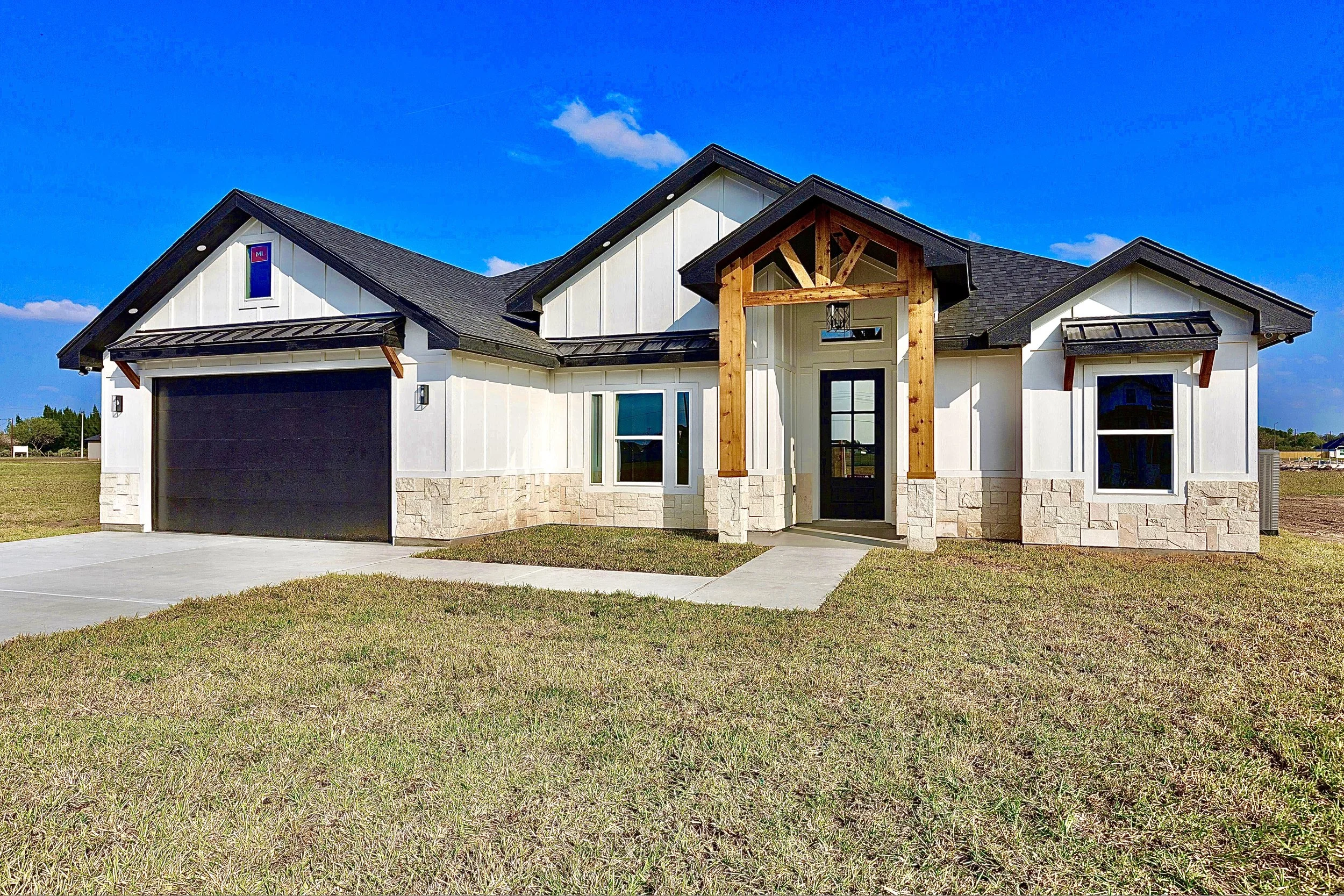 Modern suburban house with a gable roof, white exterior, stone accents, and a black garage door.