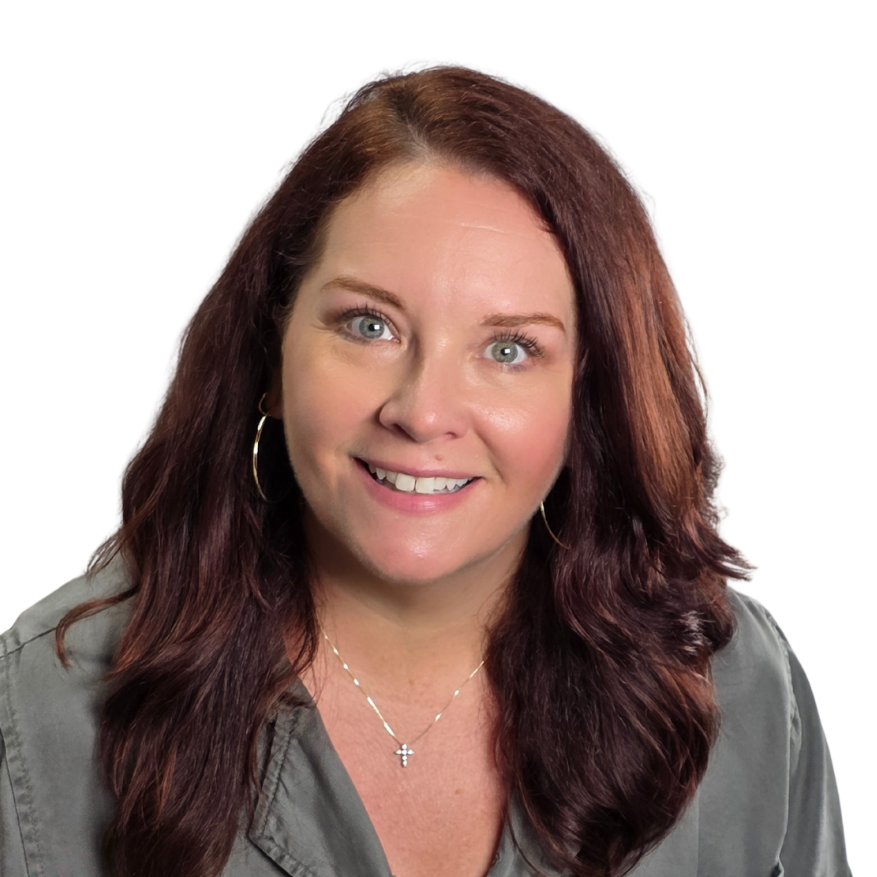 Close-up of a smiling woman with long wavy red hair, wearing hoop earrings, a necklace with a cross pendant, and a gray shirt, against a plain black background.