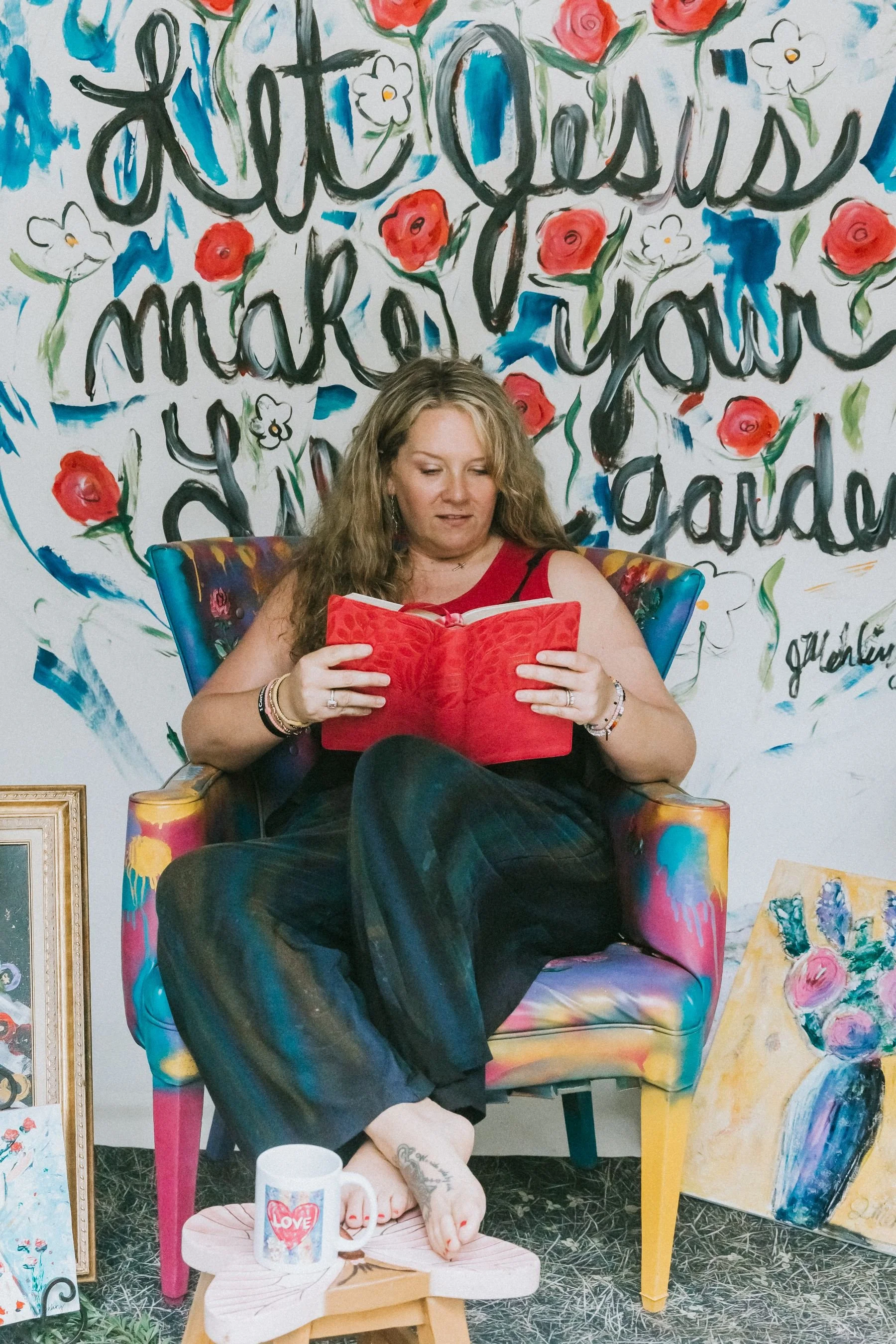 Jennifer Mehling sitting in a painted chair reading a red book, representing a quiet moment of reflection and connection with God.