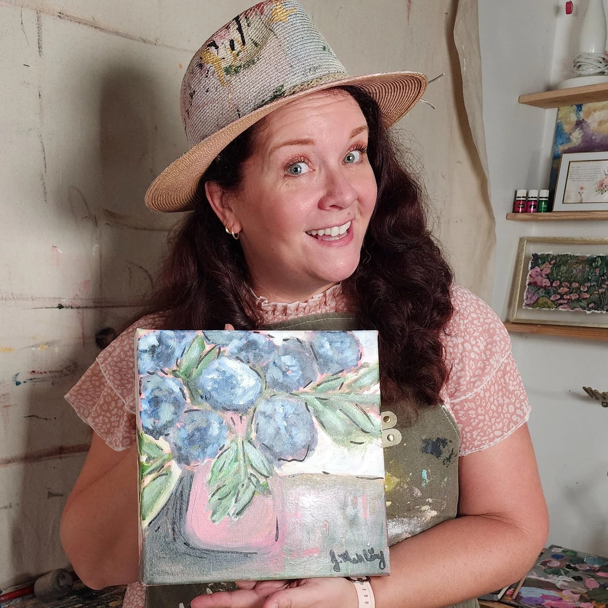 A warm photo of Jennifer with/near one of her paintings.