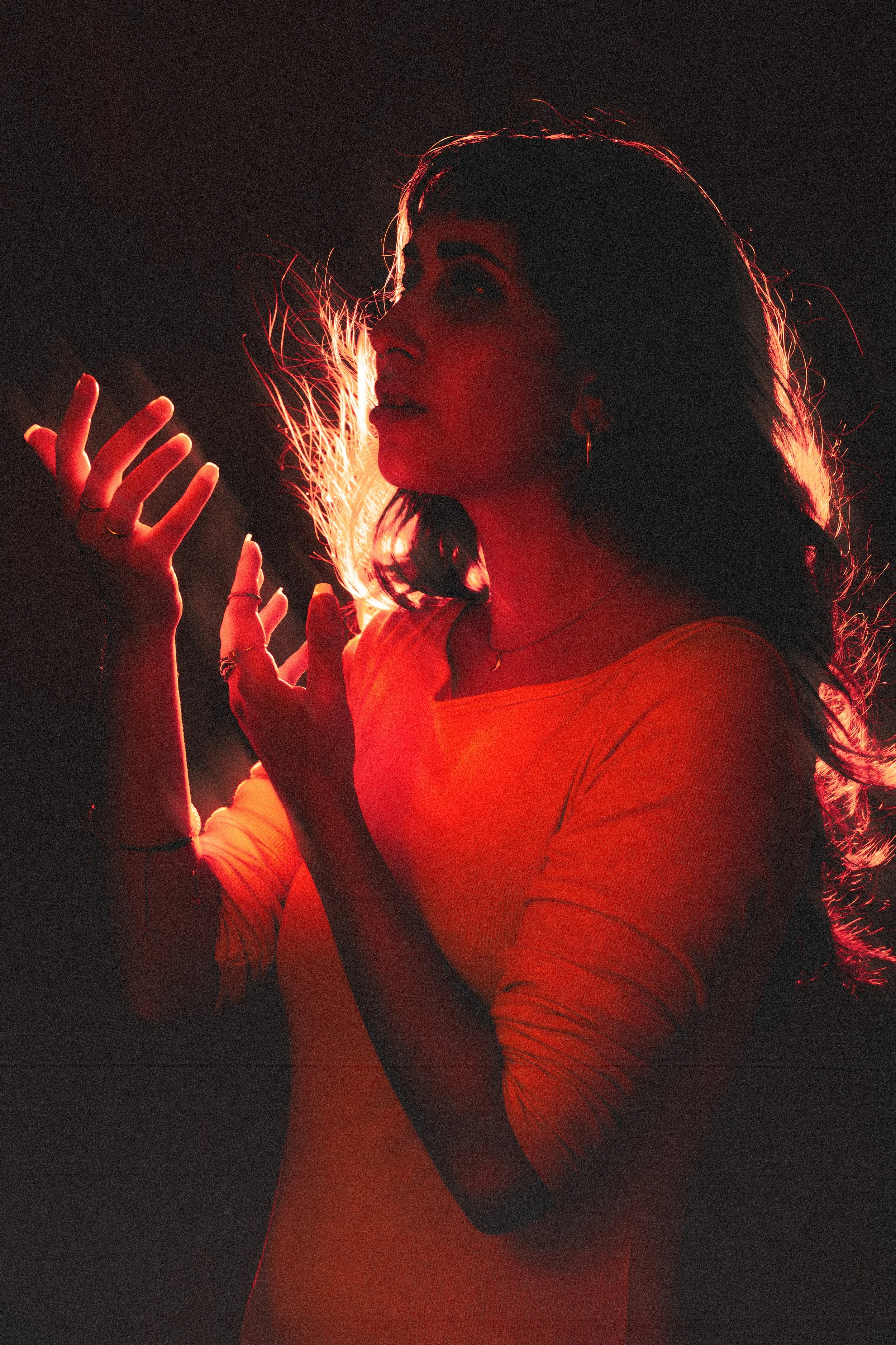 A woman with dark hair and hoop earrings, wearing a yellow top, is illuminated by a red light source, creating a dramatic silhouette effect.