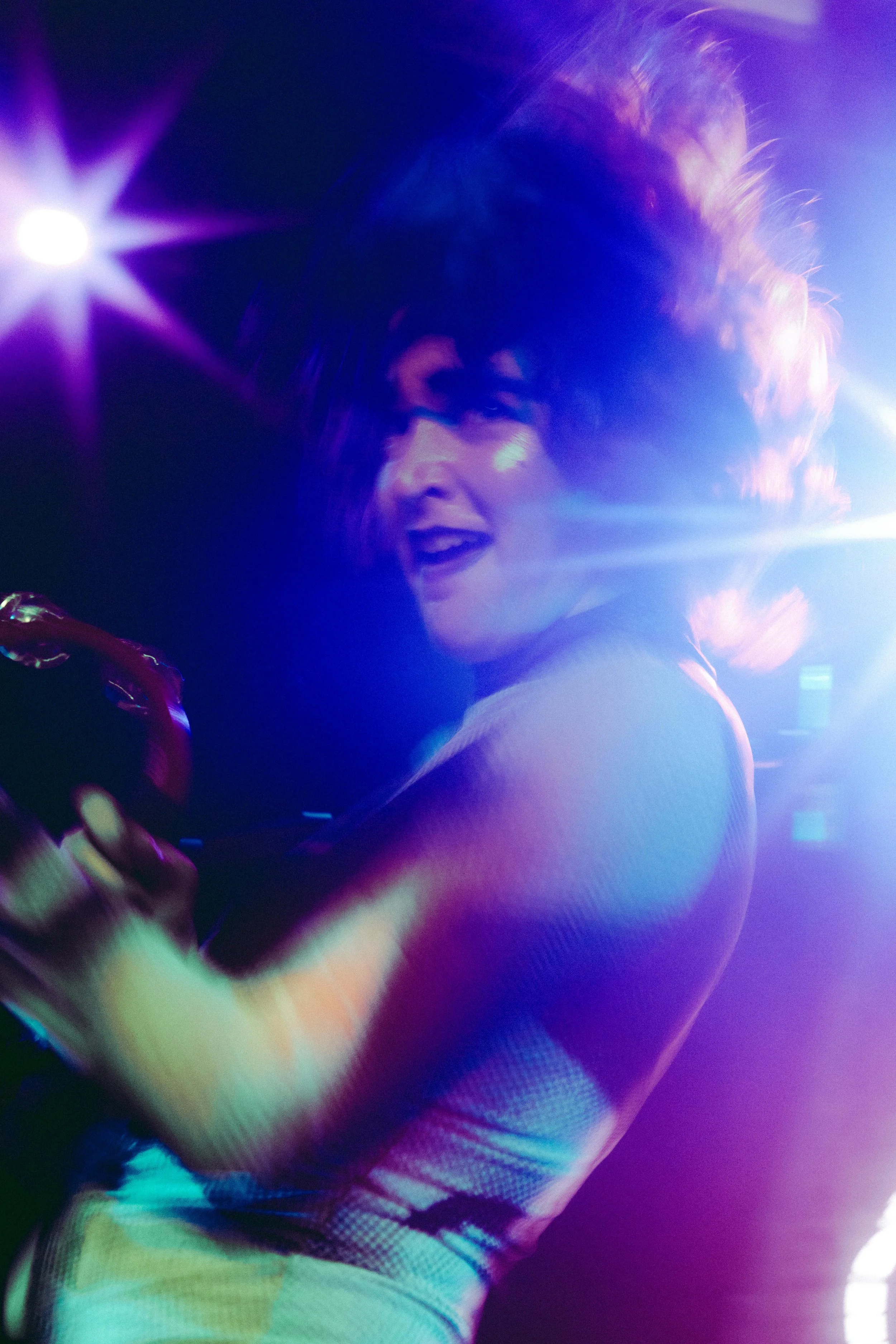 A woman with styled hair and expressive face dancing amidst colorful dance lights.