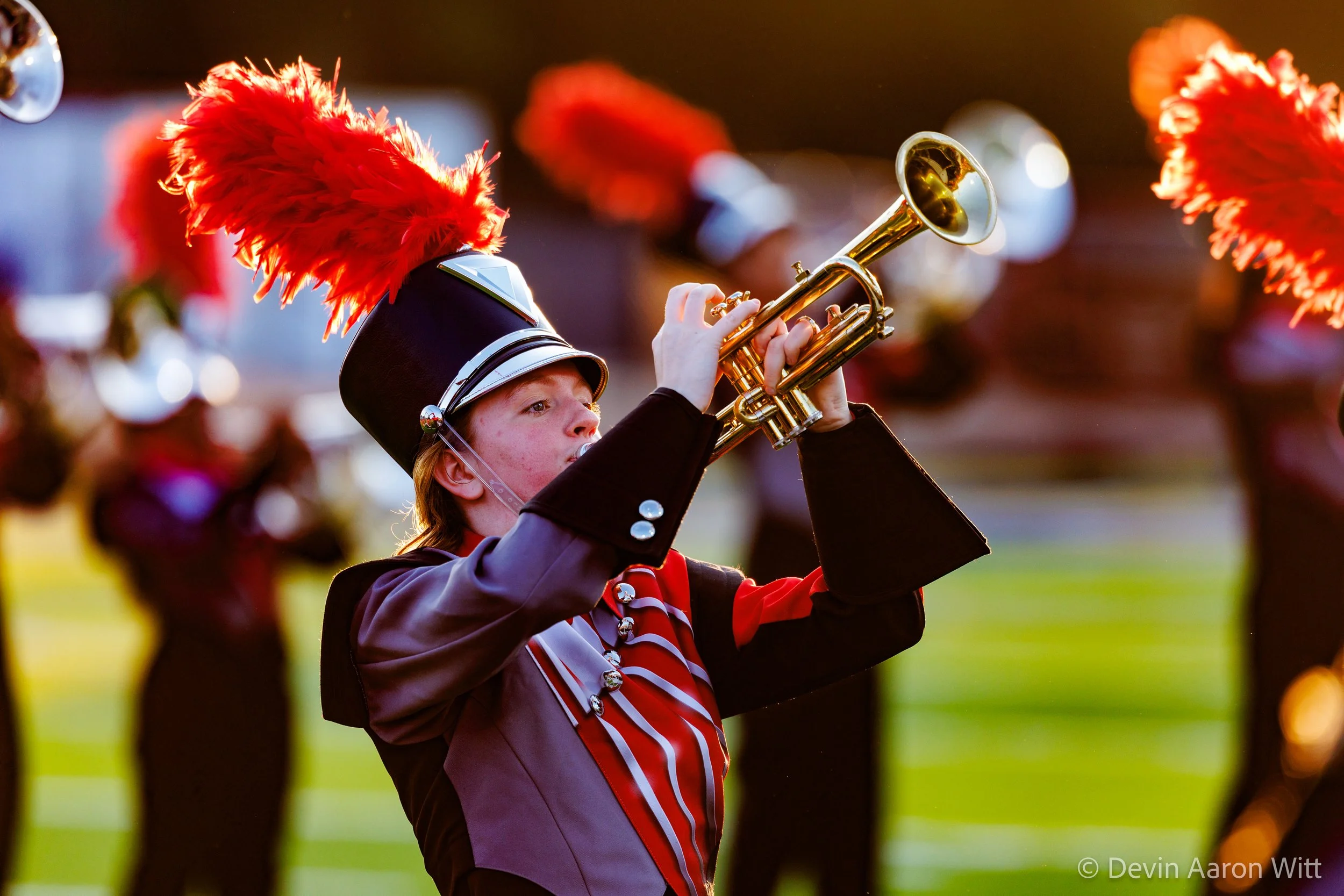 A young marching band member in uniform playing a trumpet during a parade.