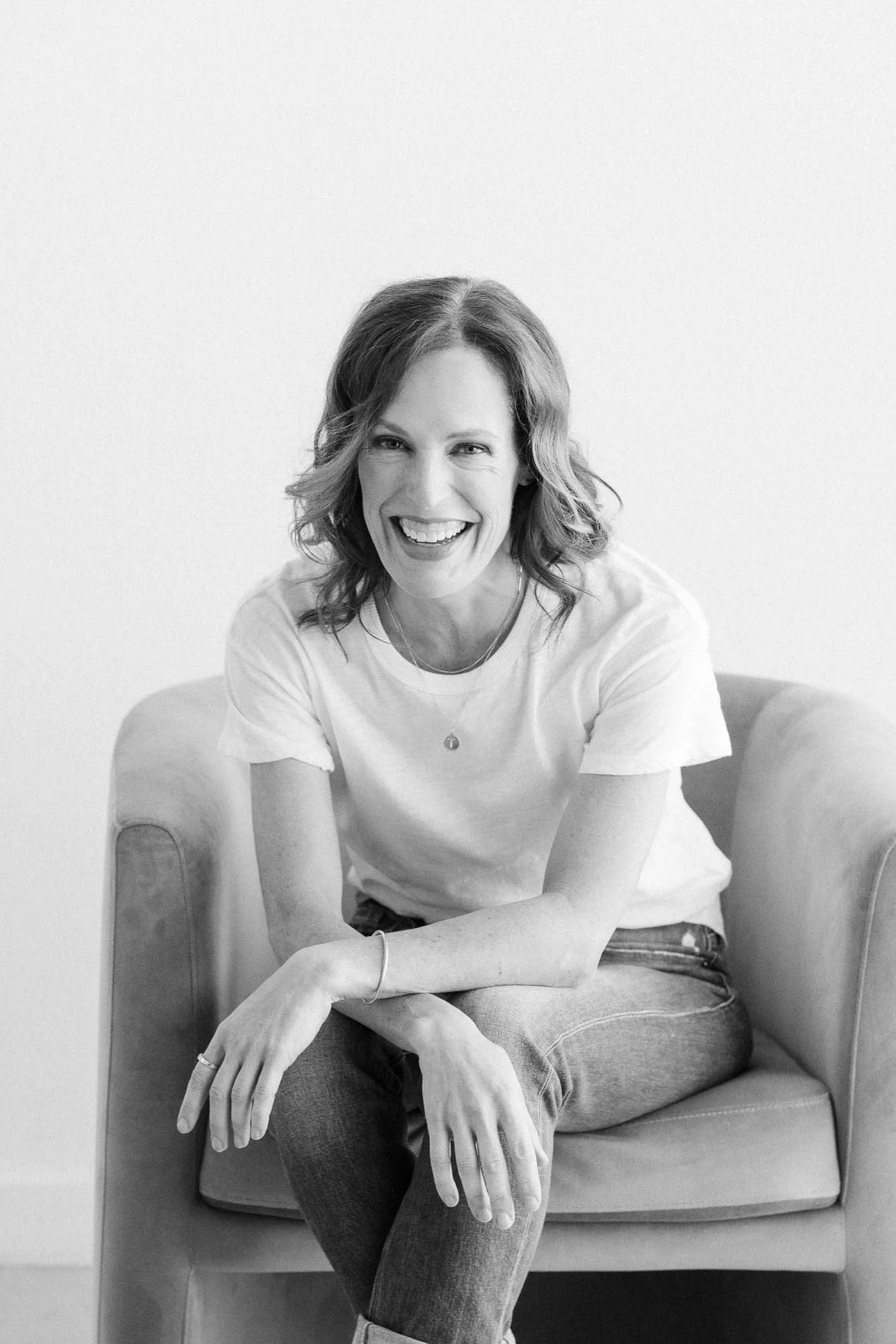 Tamara Smith, smiling and seated, leans forward in a chair while wearing casual attire.