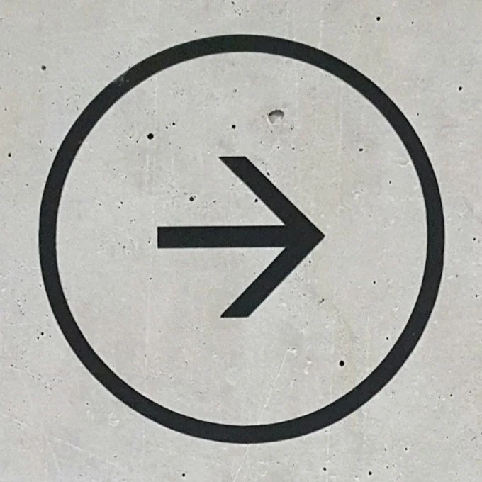 A black right arrow inside a circle, on a light gray wall.