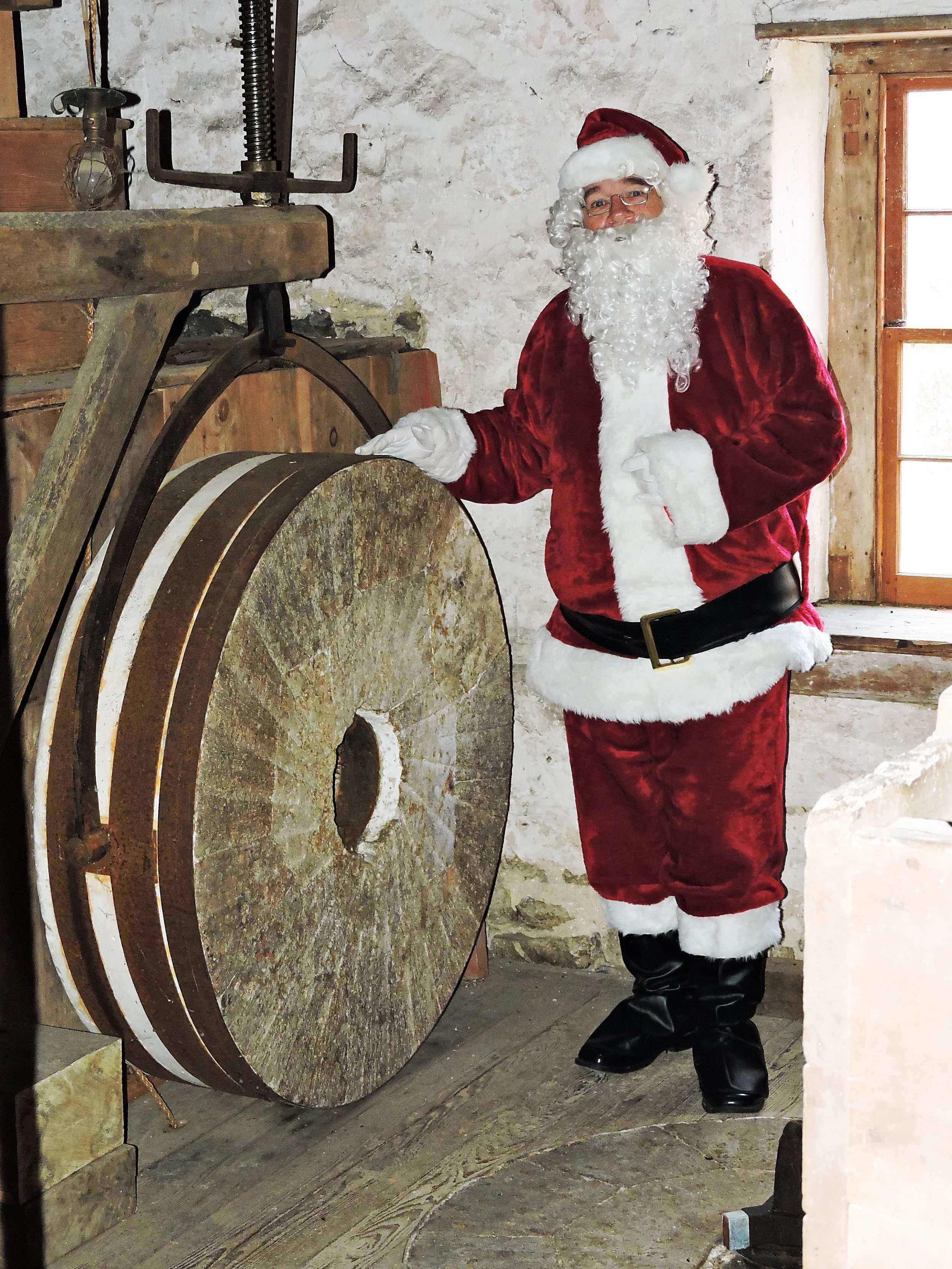 Person in Santa Claus costume standing next to an old millstone in a rustic setting.
