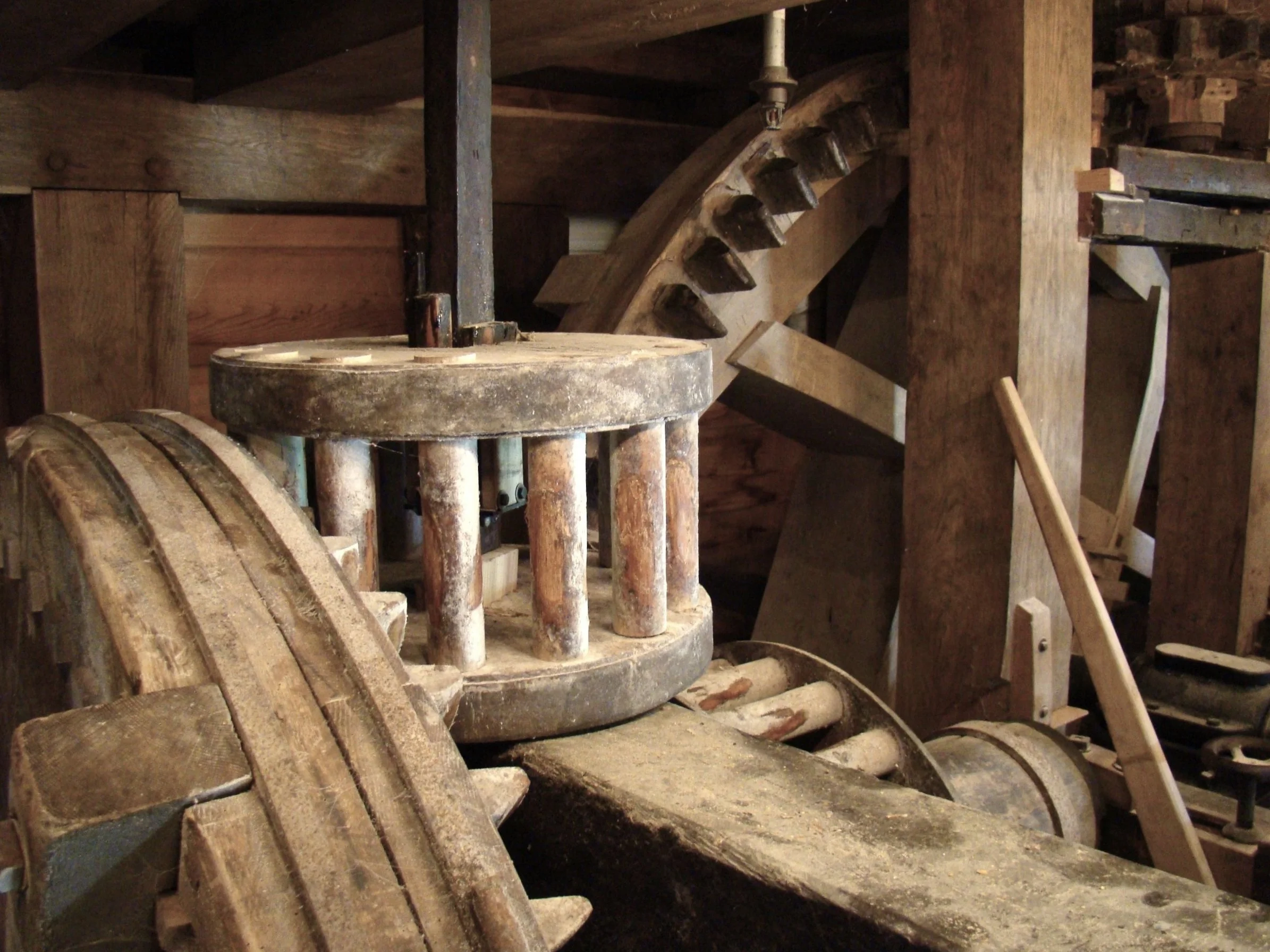 Old wooden gears and machinery inside a historic gristmill, featuring large wooden cogs and axles.