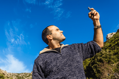 Man holding up a phone to find cell signal in the mountains