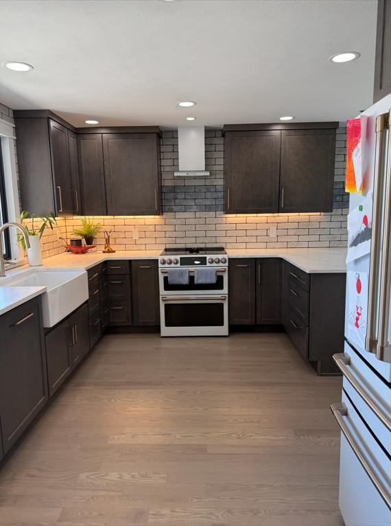 Modern kitchen with dark cabinets, white countertops, and a brick-style backsplash. Features a white stove, farmhouse sink, and a refrigerator decorated with holiday magnets. Recessed lighting installs in the ceiling.