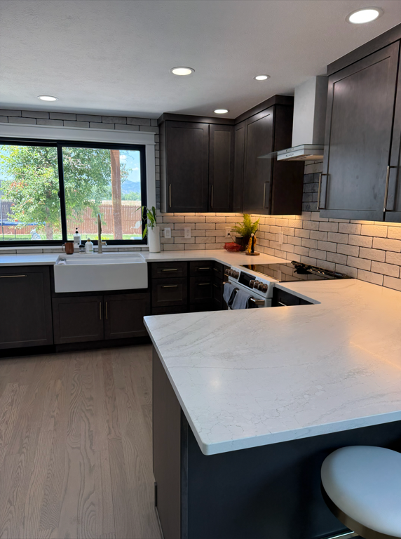 Modern kitchen with dark cabinets, white marble countertop, brick backsplash, and a large window with a view of greenery outside.