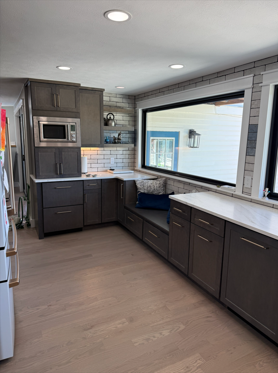 Modern kitchen with gray cabinets, white marble countertops, brick-patterned backsplash, and large window with a seating nook.