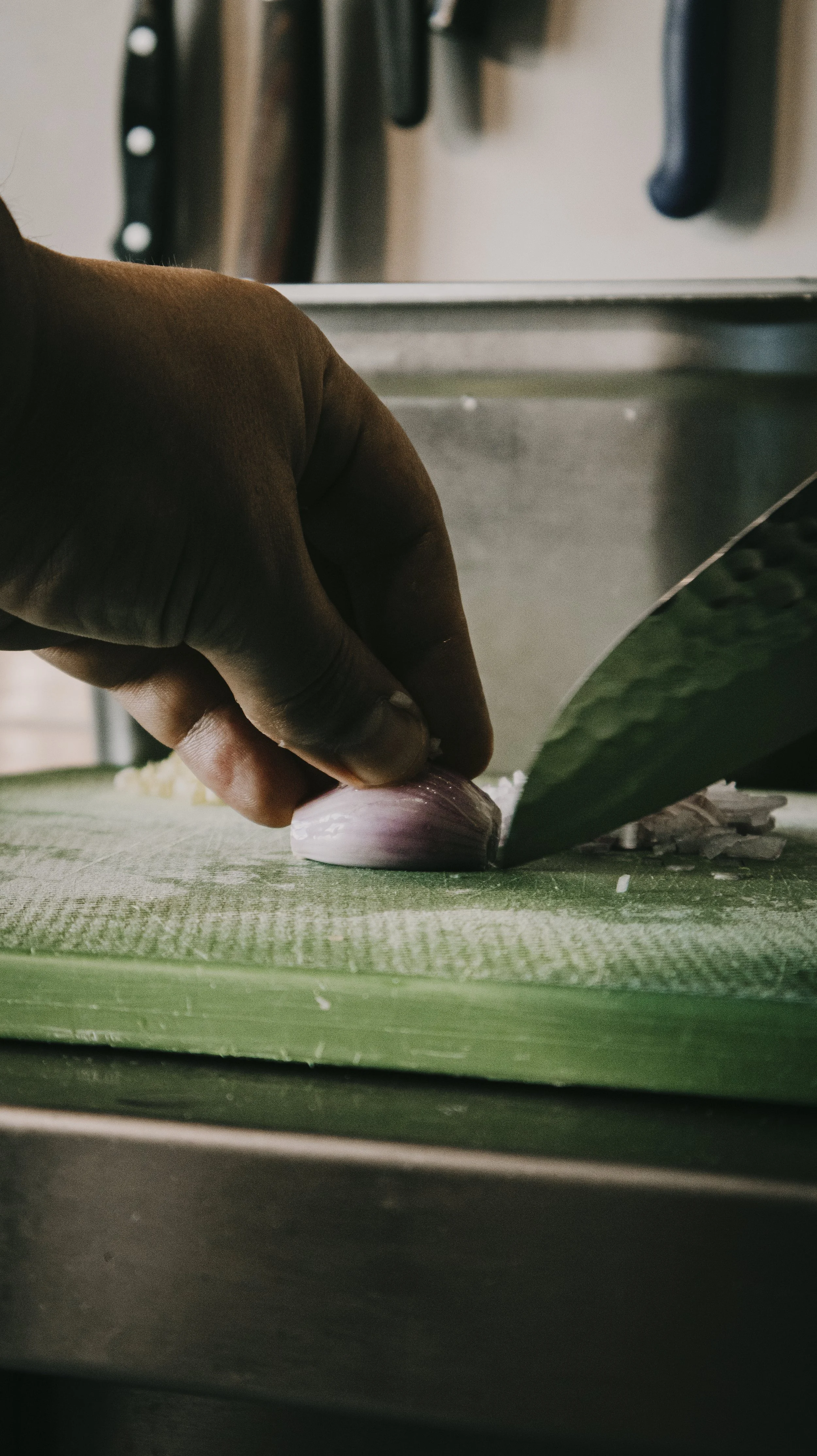 Pessoa cortando alho em uma tábua de corte verde.