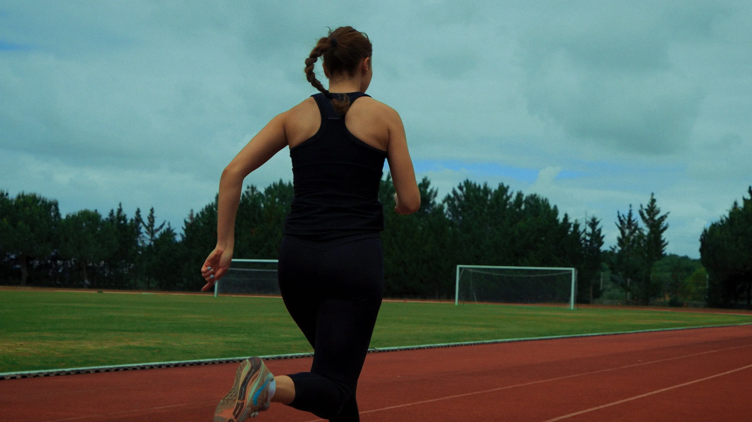 Mulher correndo na pista de atletismo ao ar livre com grama e árvores ao fundo