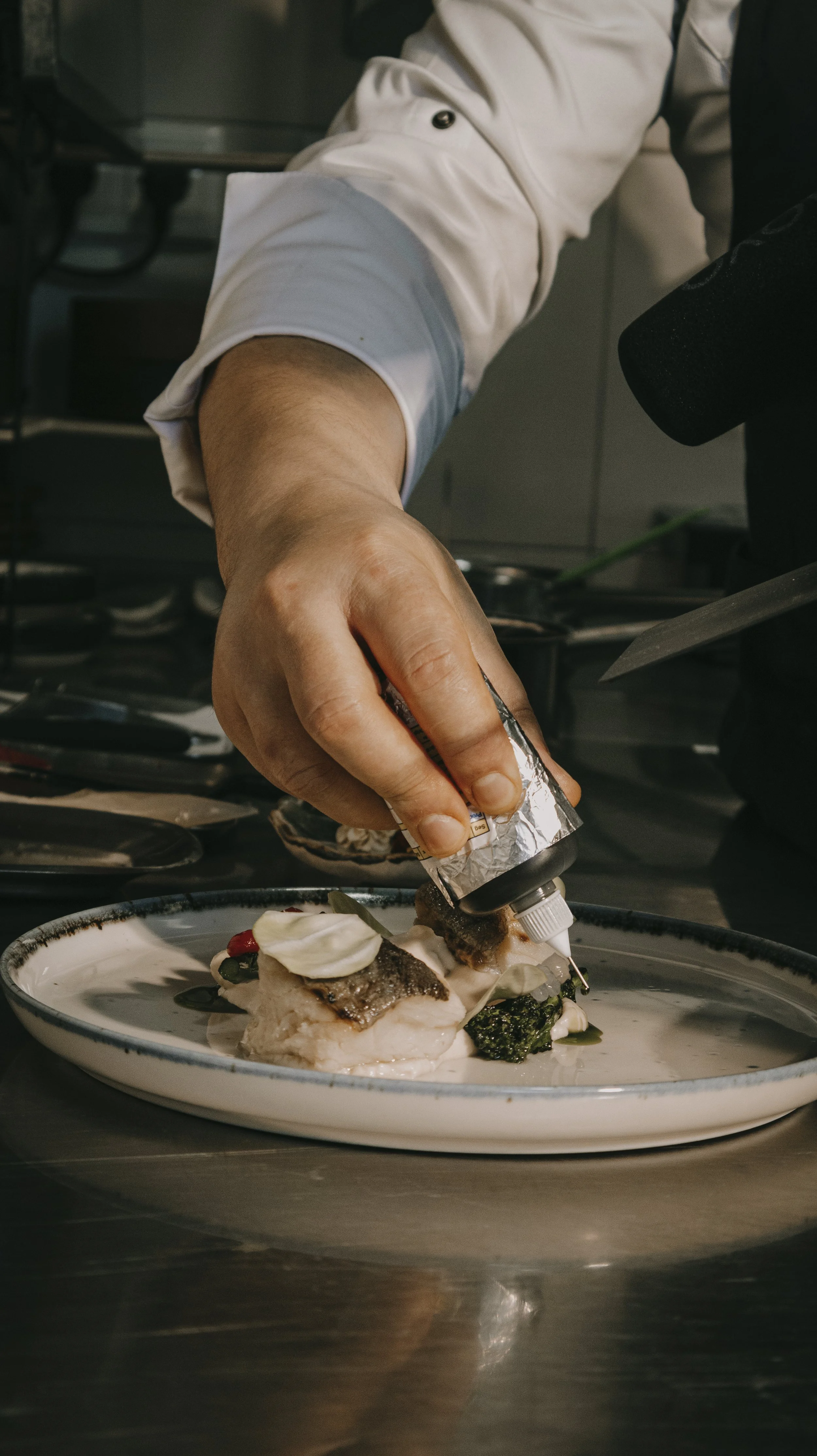 Chef colocando molho em prato de peixe com vegetais
