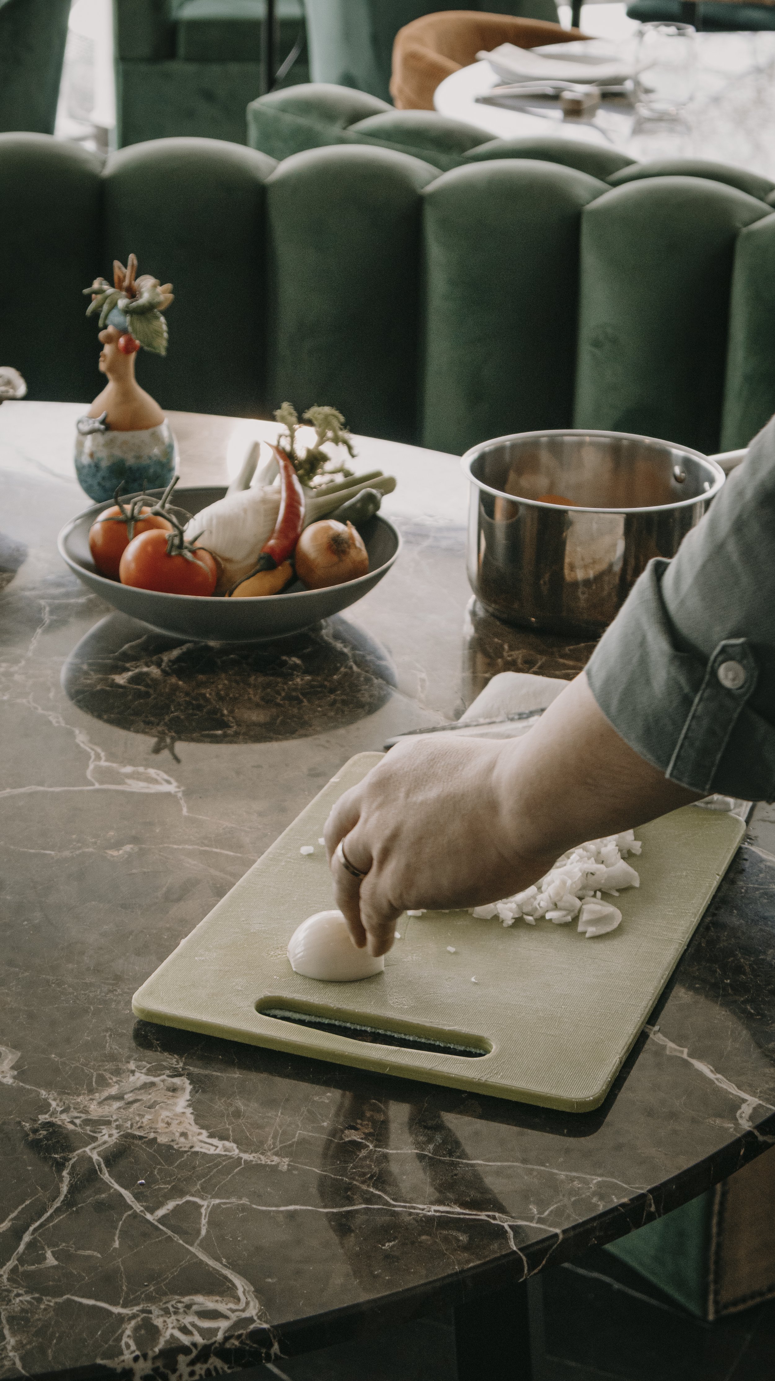 Pessoa cortando cebola em tábua de cortar em uma cozinha moderna, com tigela de legumes ao fundo e uma decoração elegante.