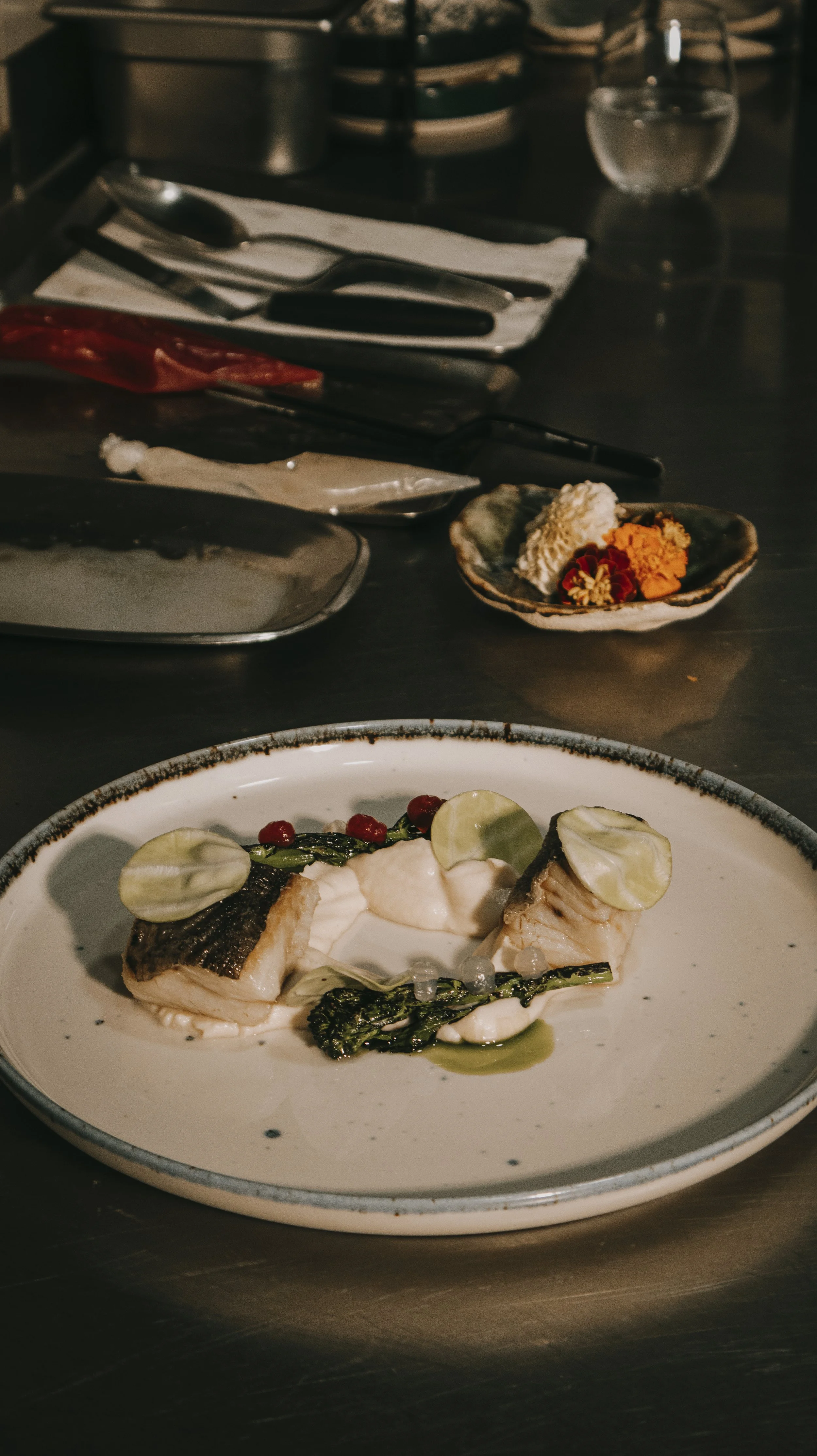 Prato com filés de peixe grelhados, acompanhados de molho branco, folhas verdes, brotos e pequenos tomates vermelhos, decorados com fatias de limão.