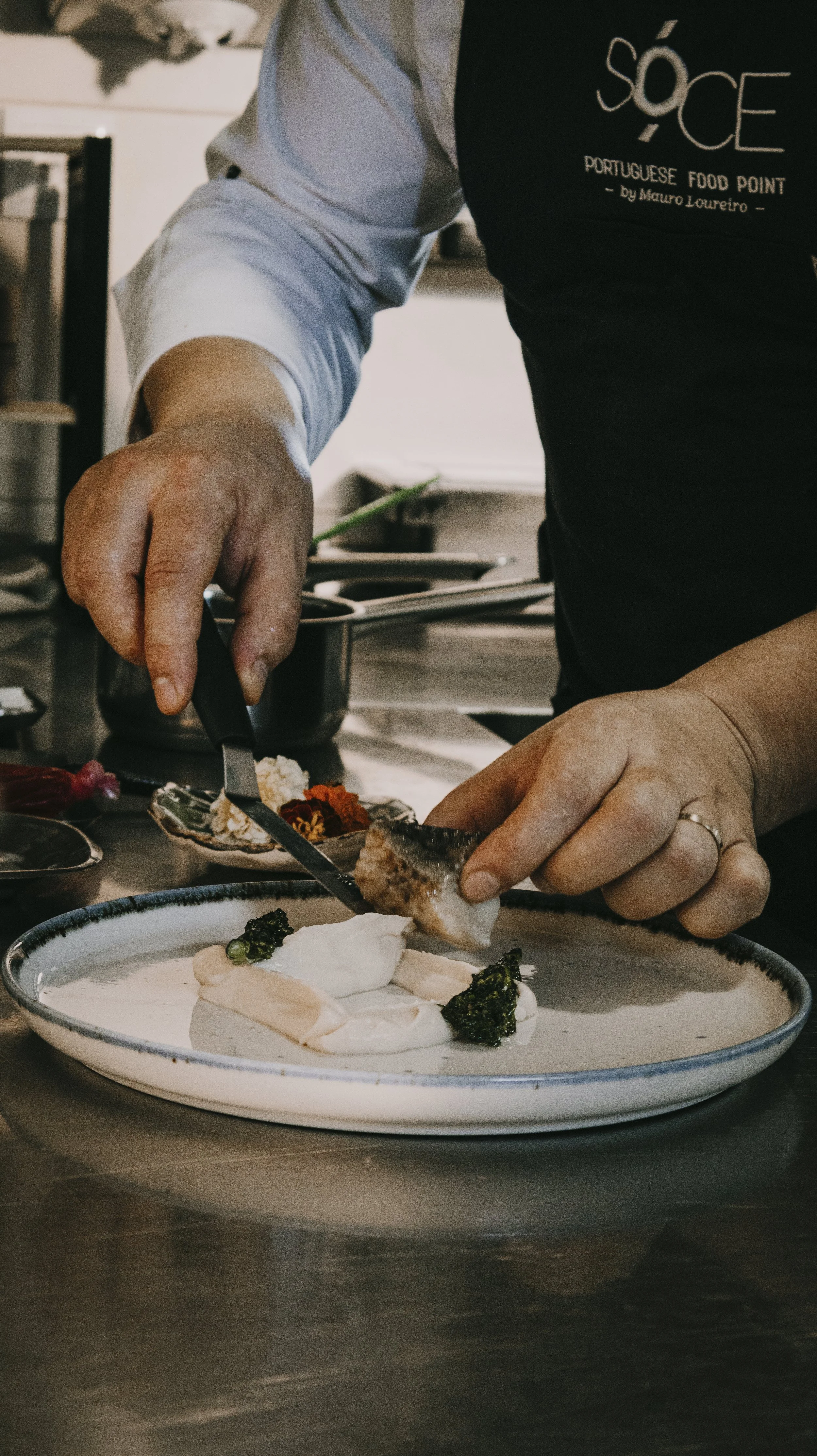 Pessoa preparando prato de comida portuguesa, colocando peixe e guarnições em uma bandeja
