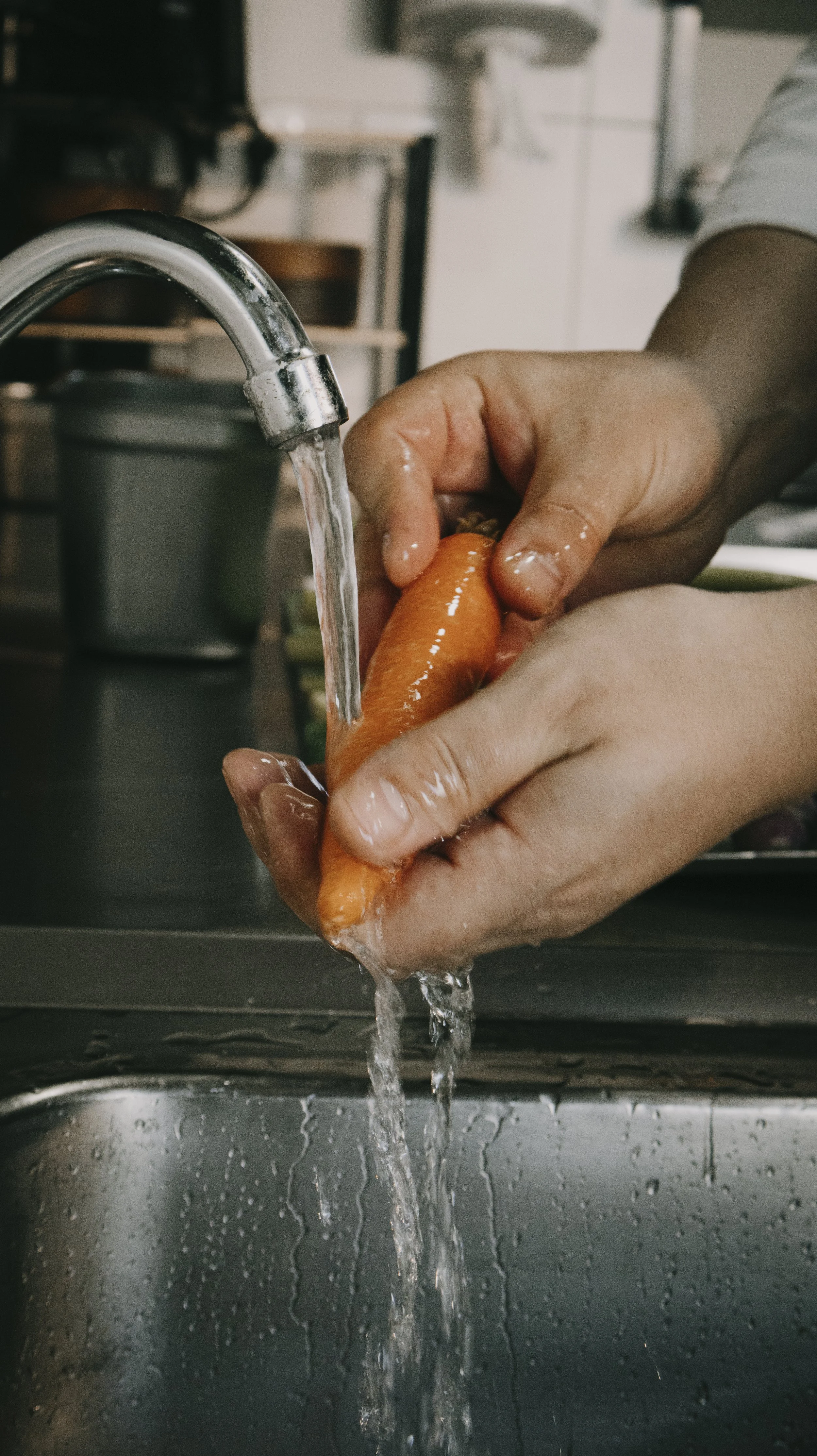 Pessoa lavando uma cenoura sob água corrente em uma pia de cozinha.