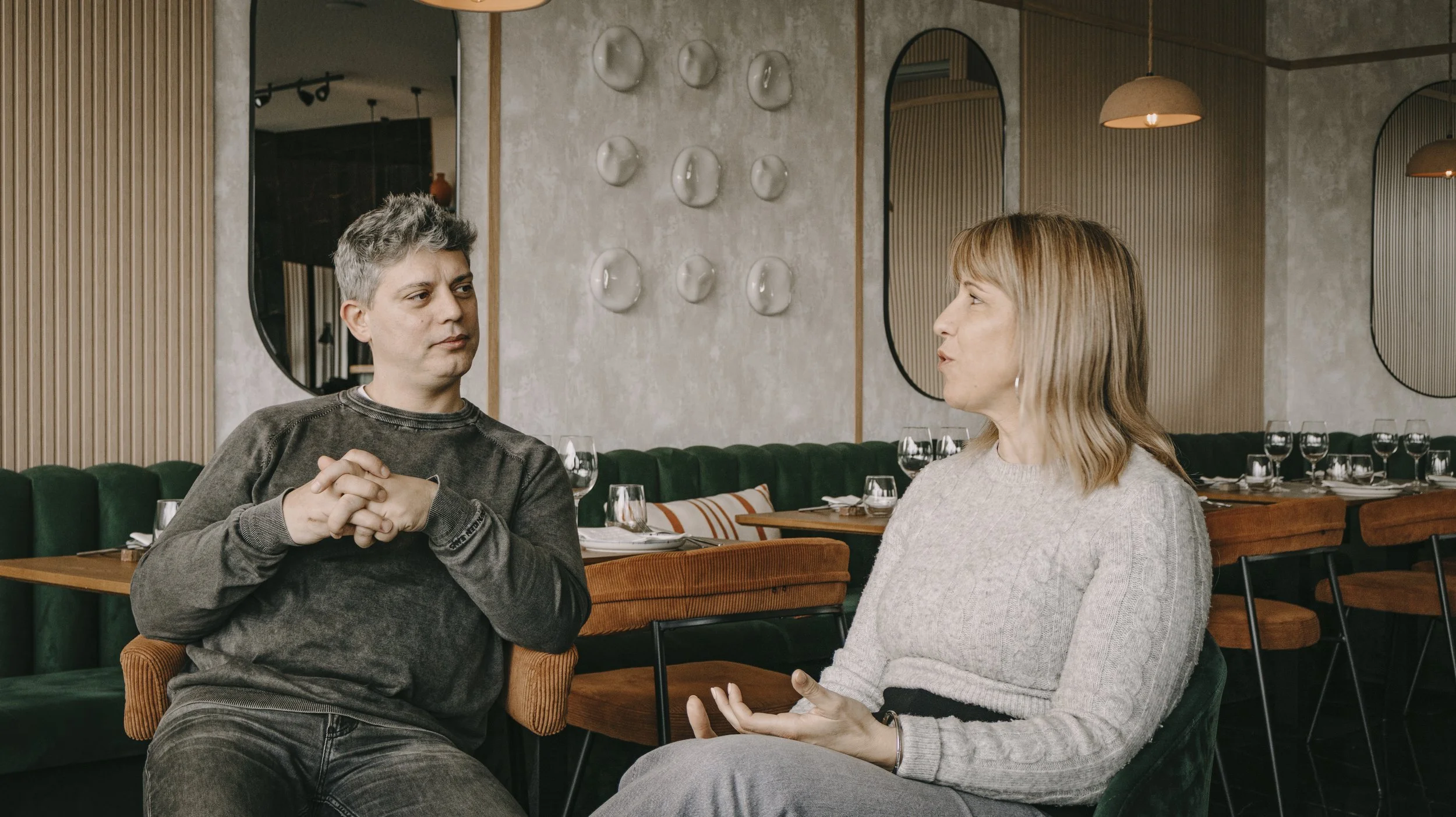 Homens e mulher conversando em um restaurante decorado com espelhos e paredes de cimento.