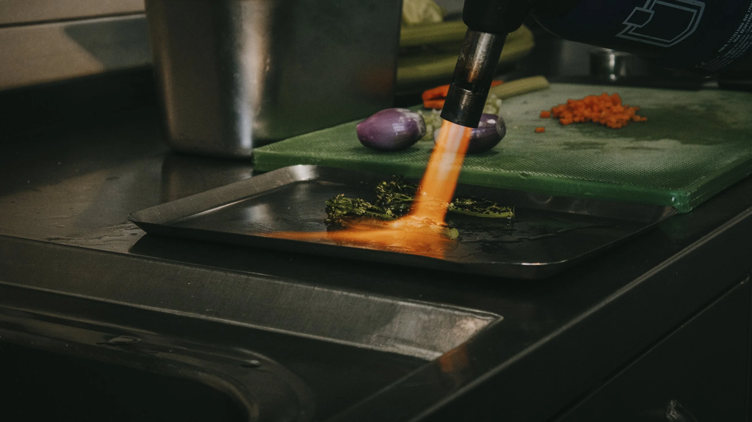 Chef usando um maçarico para tostar ou caramelizar alimentos na cozinha de um restaurante.