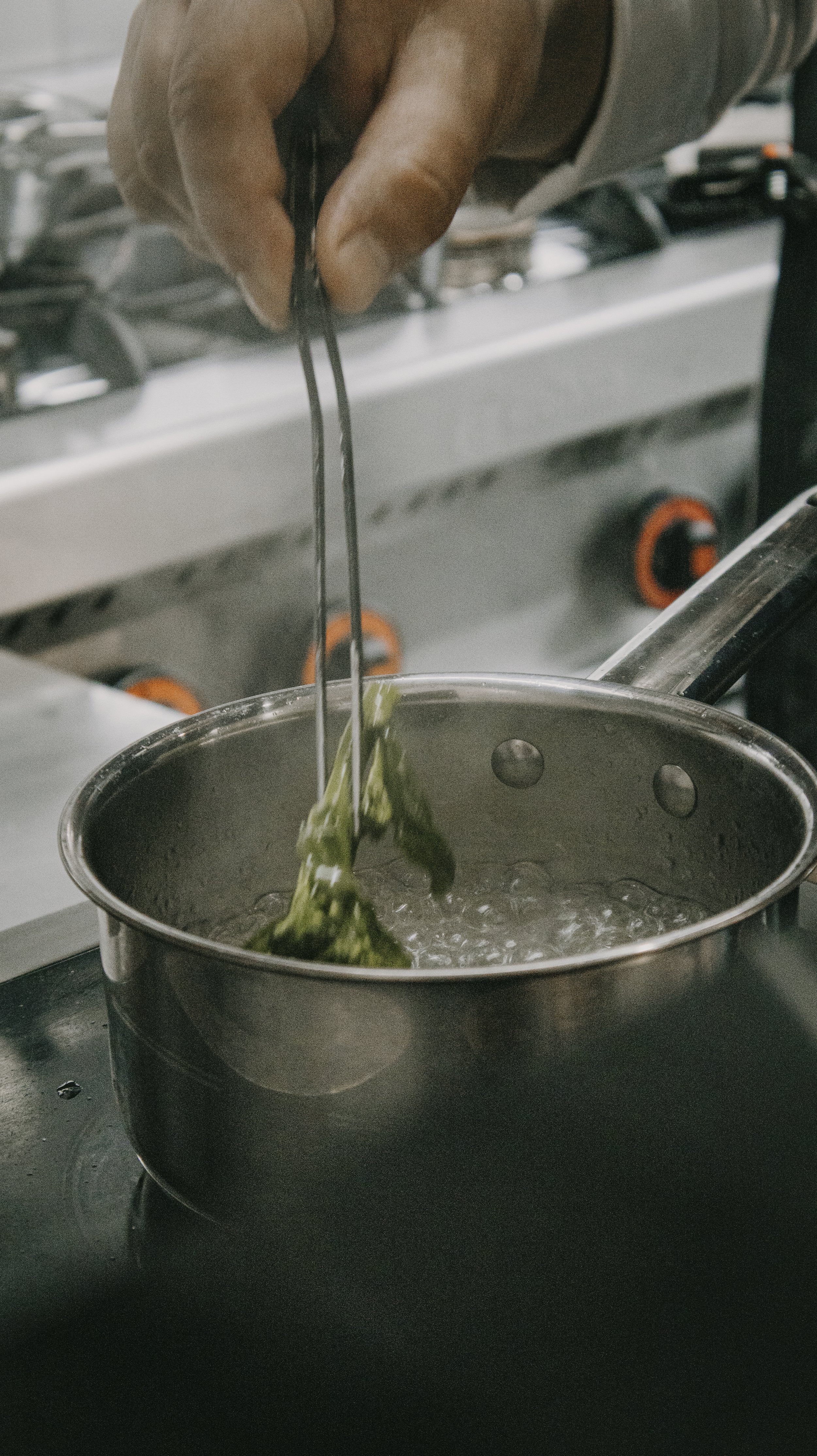 Pessoa adicionando aspargos ao fervedor de água para cozinhar em uma cozinha profissional.