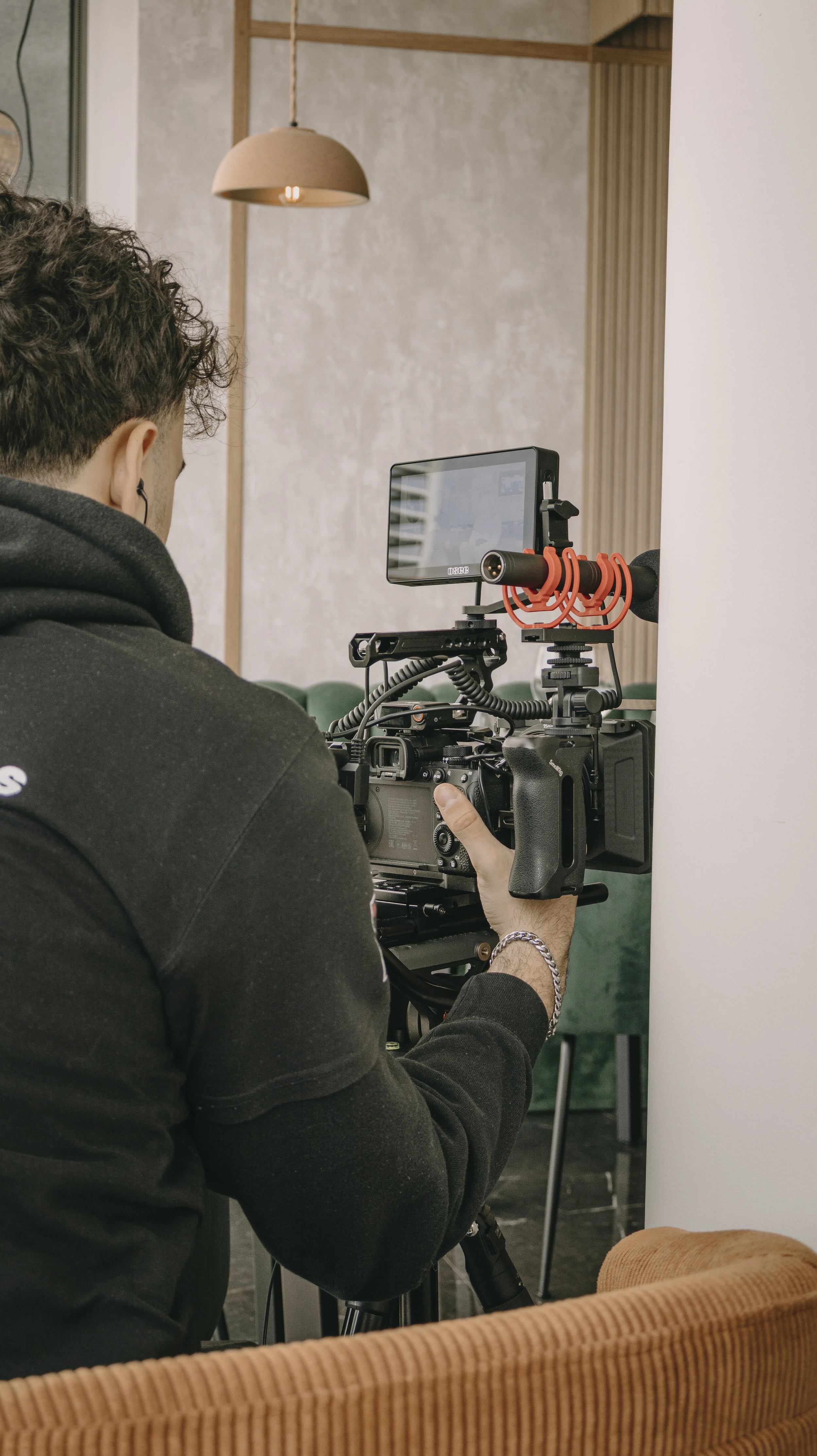 Pessoa operando uma câmera de vídeo em um ambiente interno, com equipamentos de filmagem e uma tela de monitor